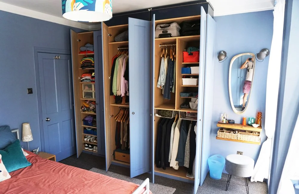Open blue wardrobes filled with clothes, shoes, and storage boxes in a bedroom with blue walls.