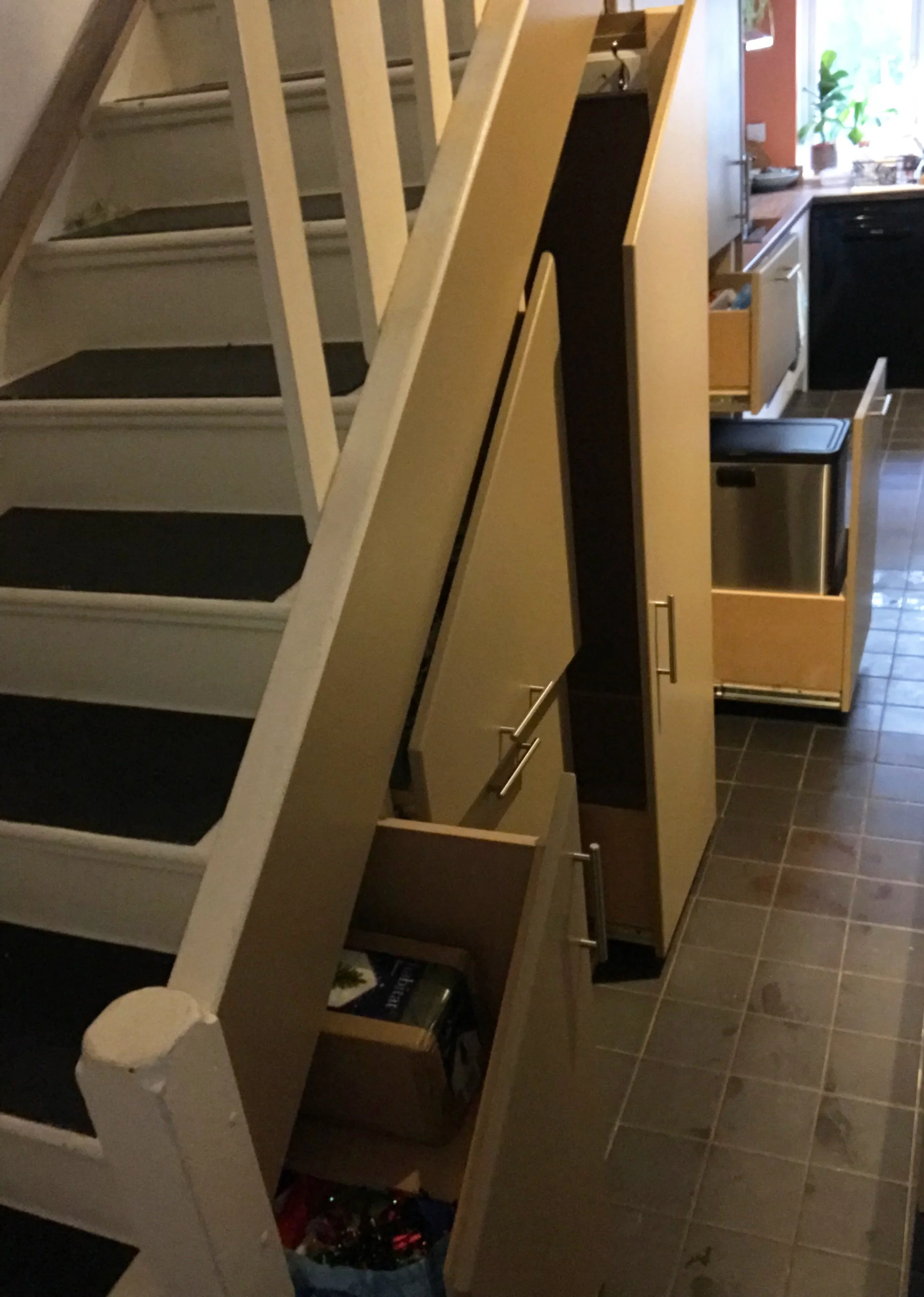 View of a staircase with black anti-slip treads, and adjacent kitchen cabinets and drawers in a home kitchen with tiled floor.