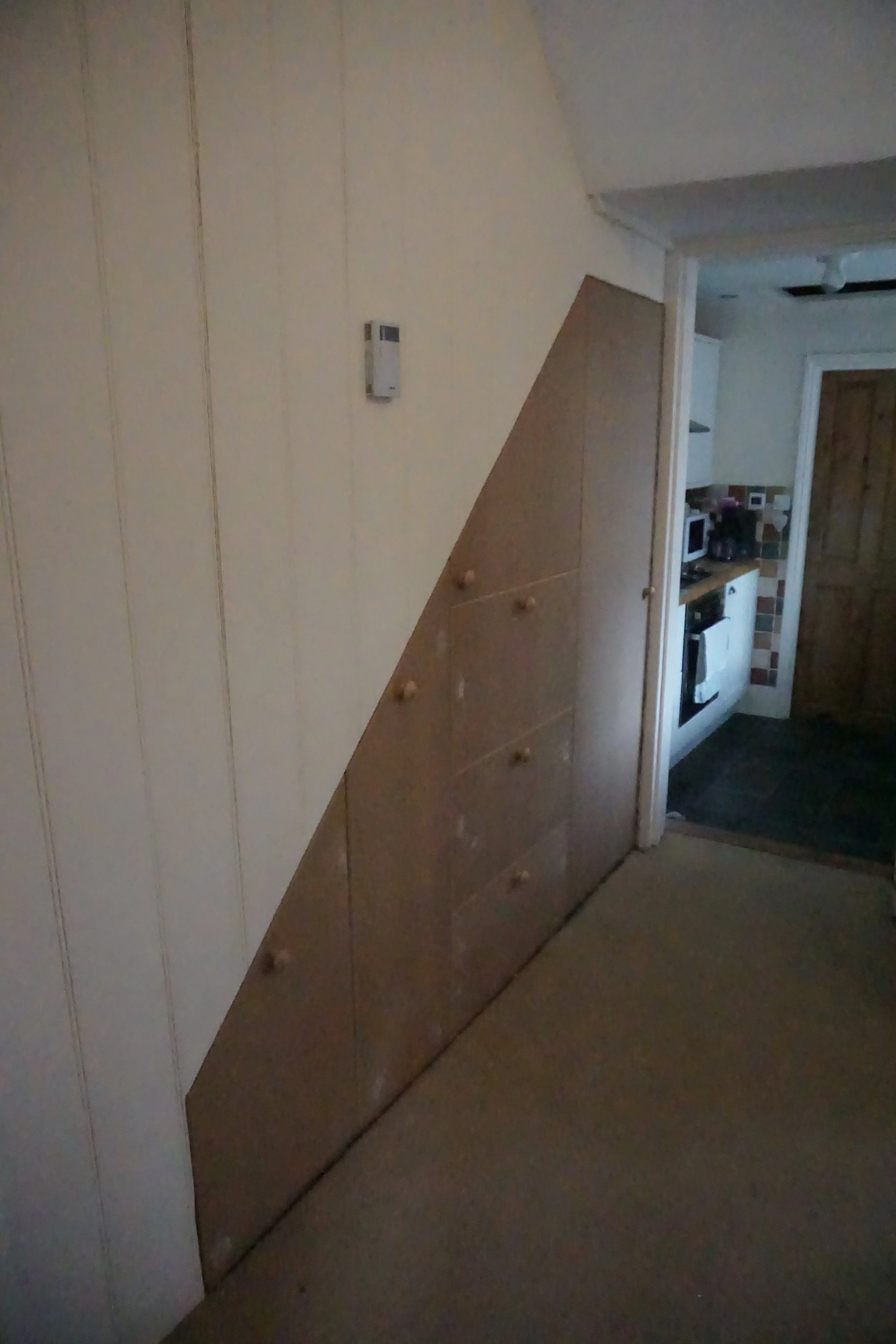 Built-in wooden storage cabinet with multiple drawers and knobs in a room with a sloped ceiling and a visible thermostat on the wall.