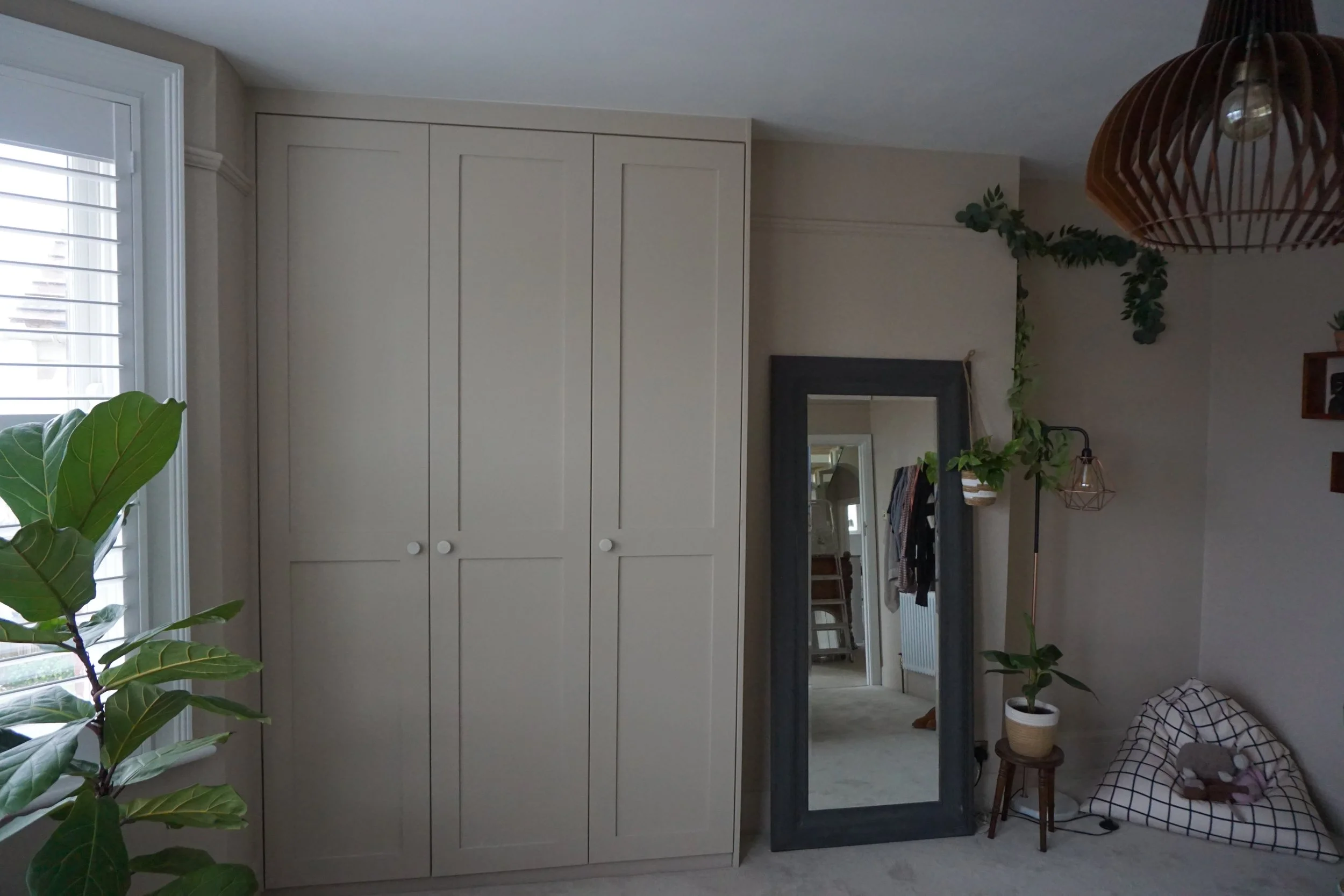 Interior of a room with a large white wardrobe, a full-length mirror, a potted plant, and a cozy pet bed with toys on a plush carpet.