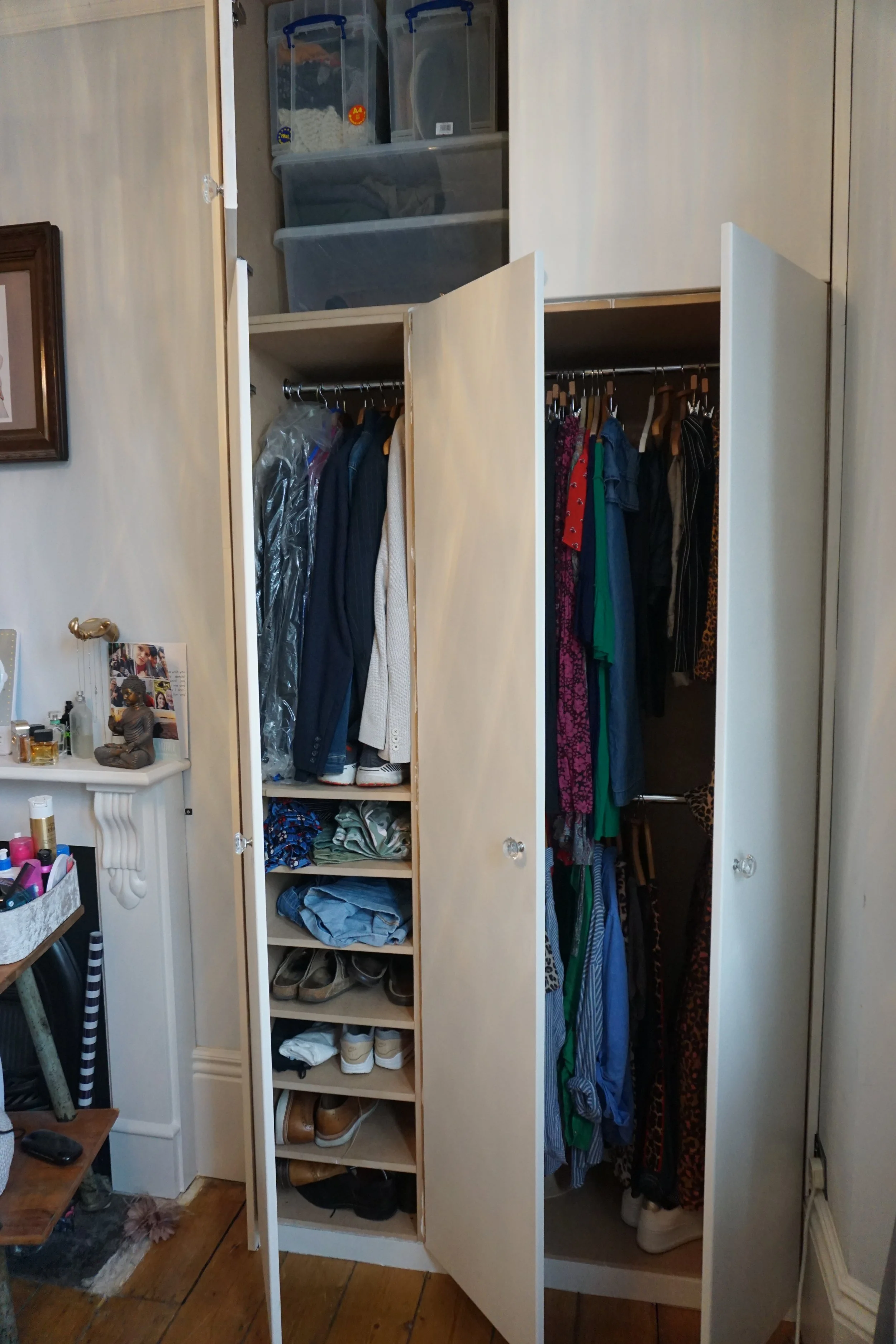 Open closet with clothes hanging on two sides, shoes on shelves at the bottom, and storage containers on top.