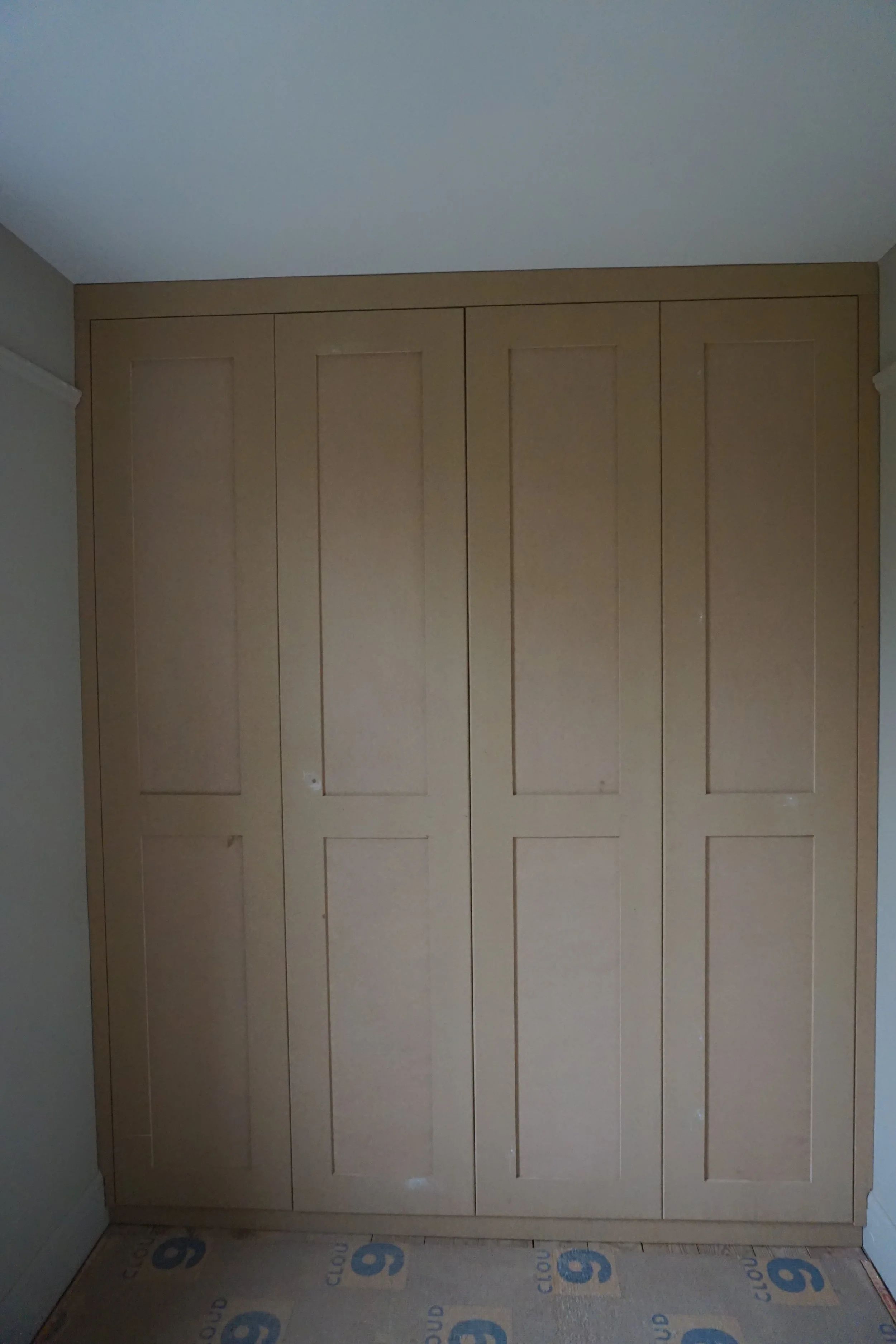 Wooden built-in closet with four doors in a room with light-colored walls and ceiling.