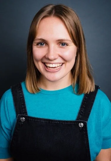 A smiling white woman with fair hair wearing dungarees