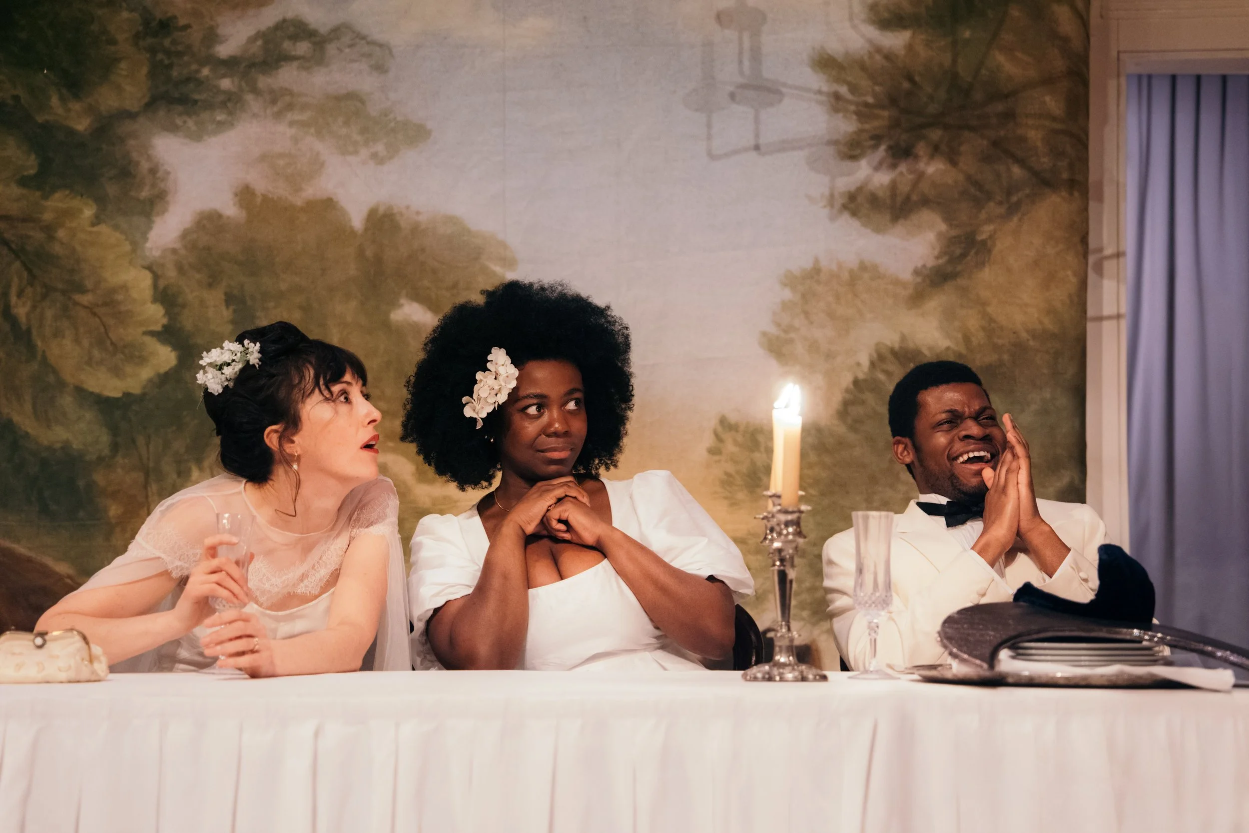 Performers in A Midsummer Night's Dream, seated at a banquet table, looking surprised and laughing