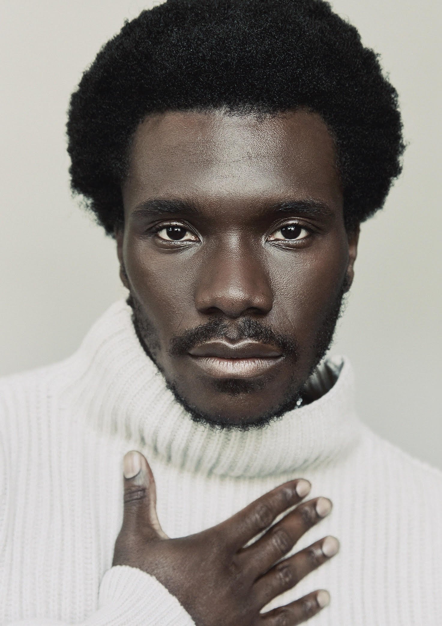 A young black man with a short afro wearing a cream turtleneck sweater