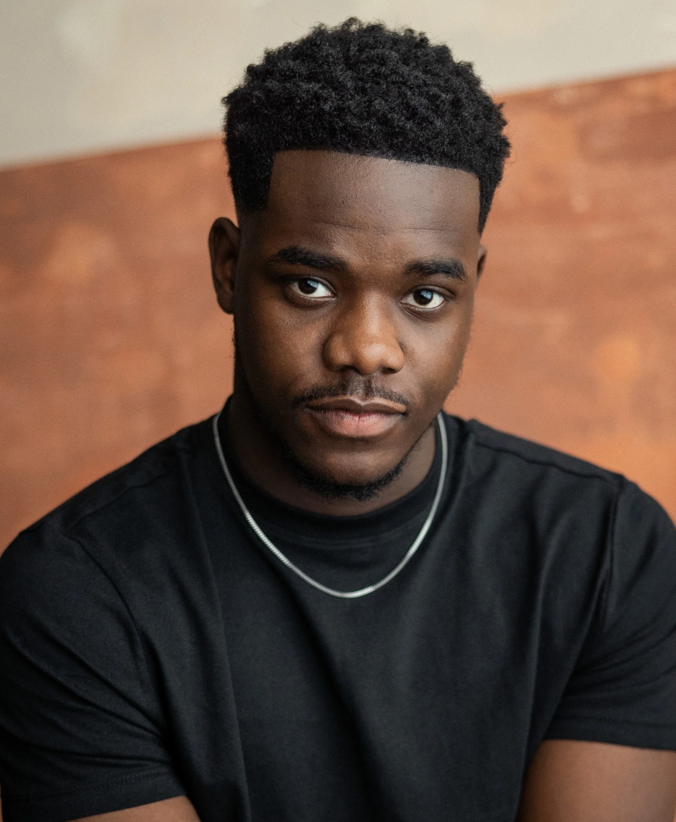 A young black man with short hair, a black shirt and silver chain