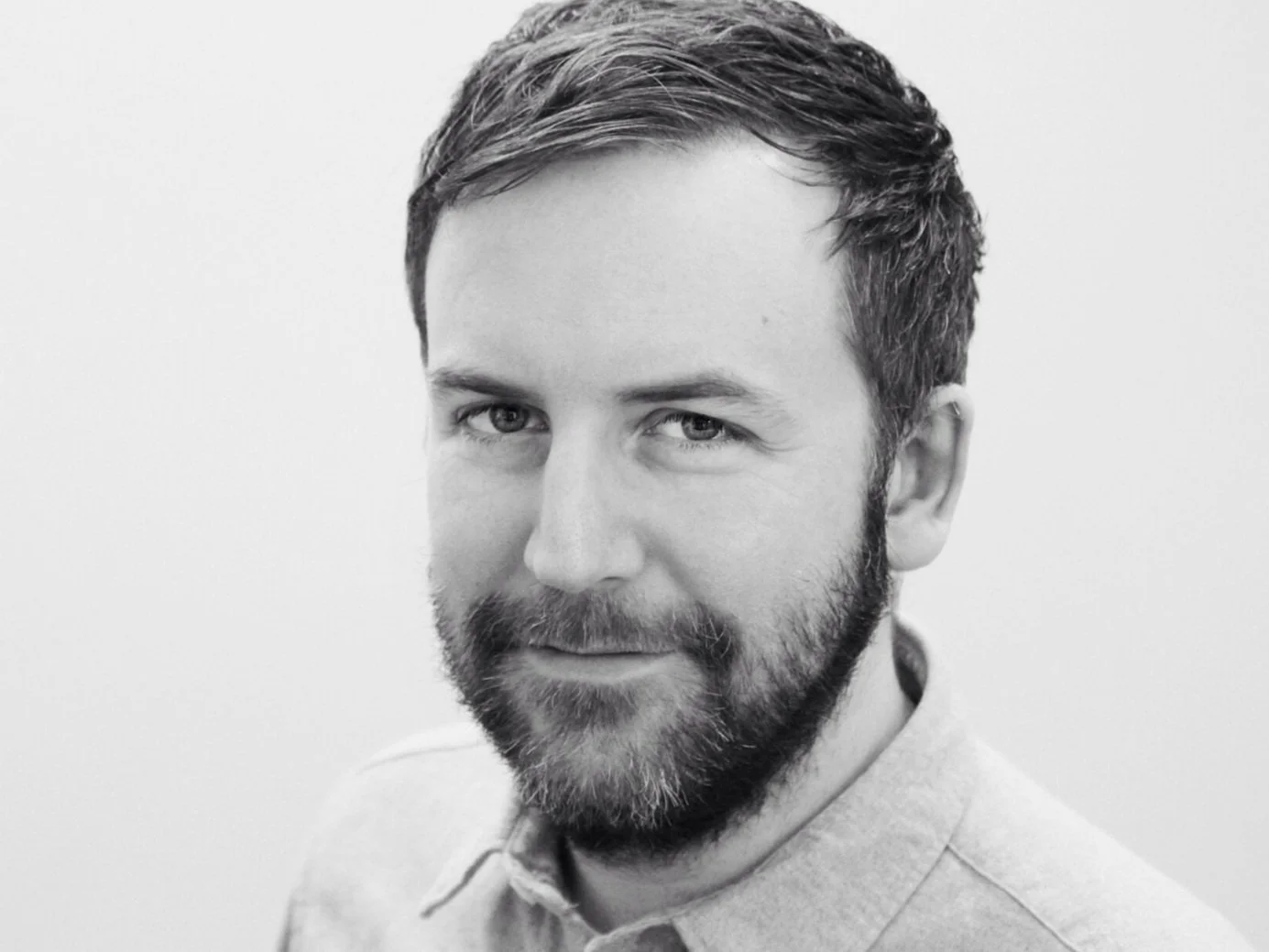 Black and white portrait of a man with short hair and a beard, wearing a collared shirt, looking at the camera