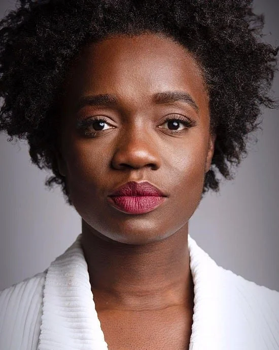 A black woman with a white shirt and red lip. She has a short textured afro.