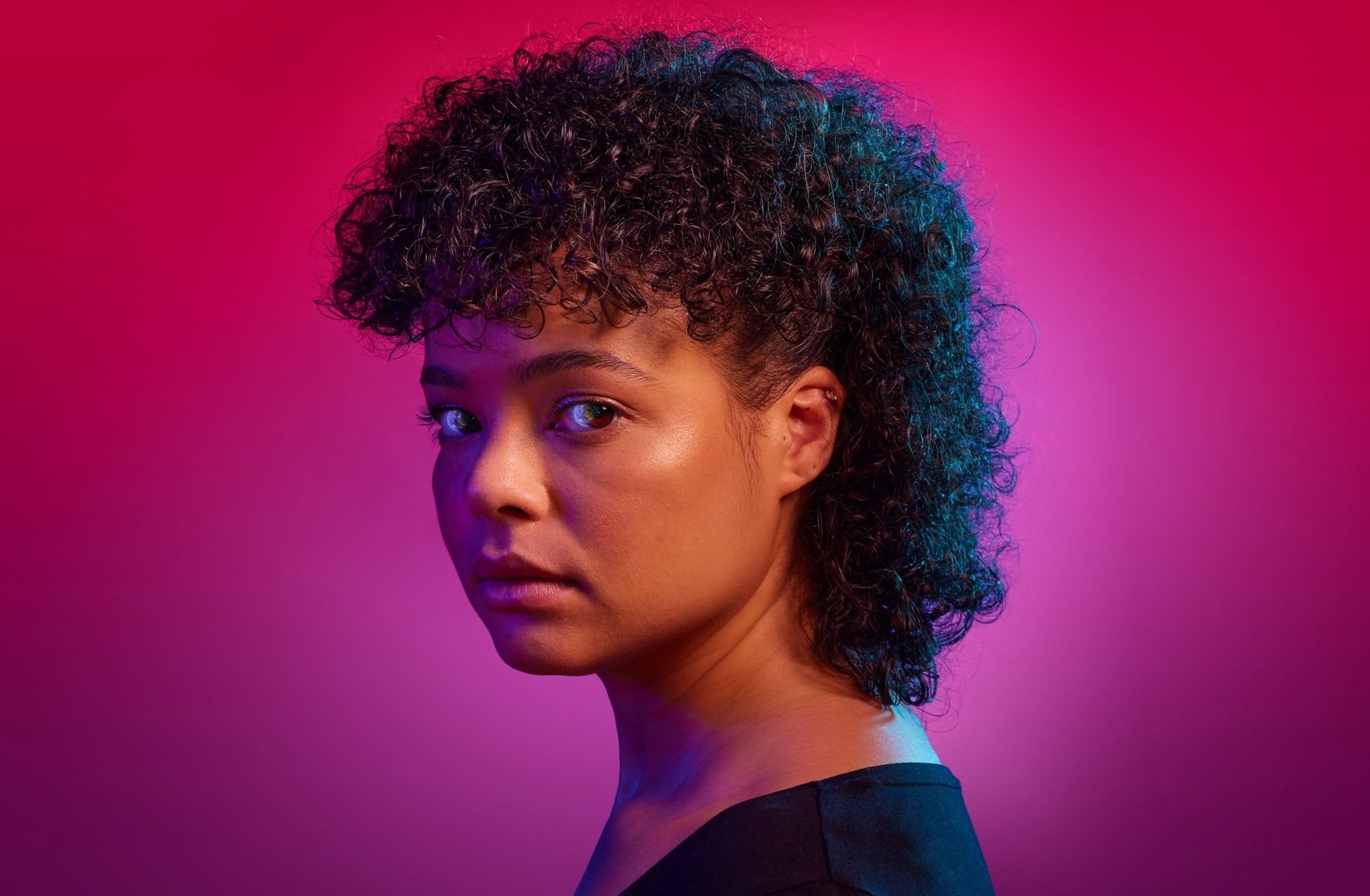 Portrait of a woman with short curly hair against a pink and purple gradient background.