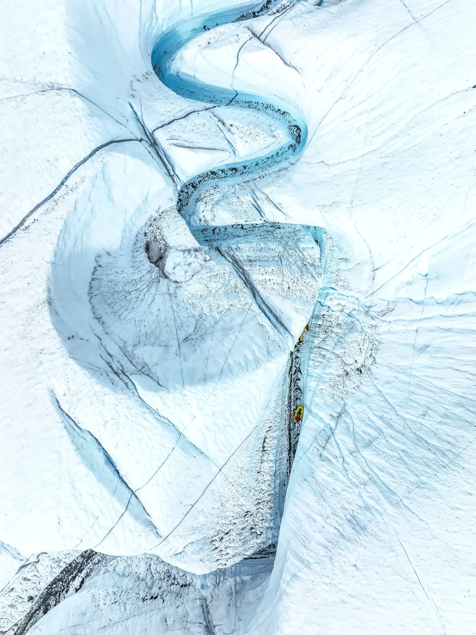 Aerial view of a winding glacier creek flowing through an icy landscape with snow-covered terrain.