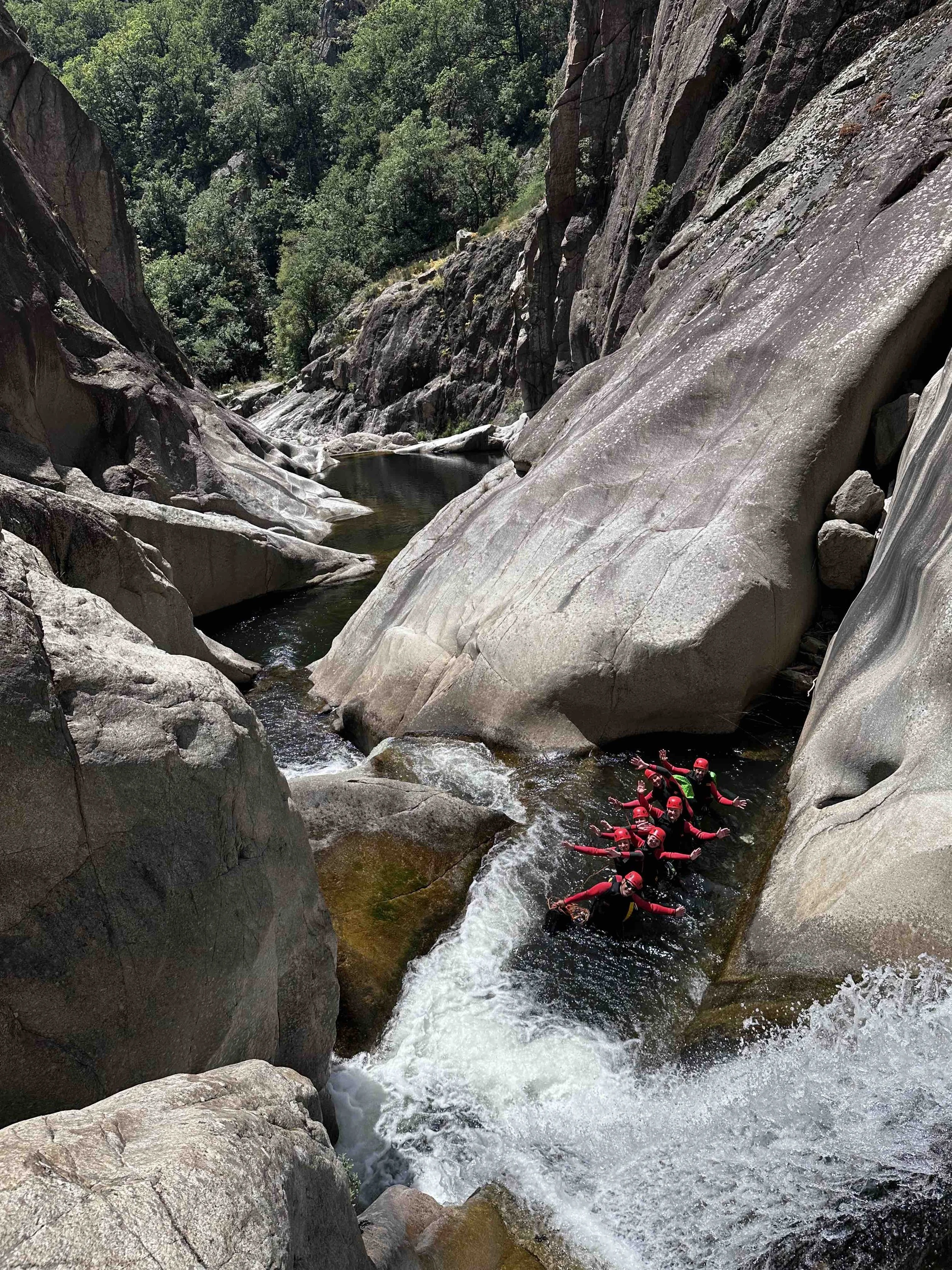 Groupe de personnes faisant du canyoning dans une rivière entourée de rochers et de végétation montagneuse.