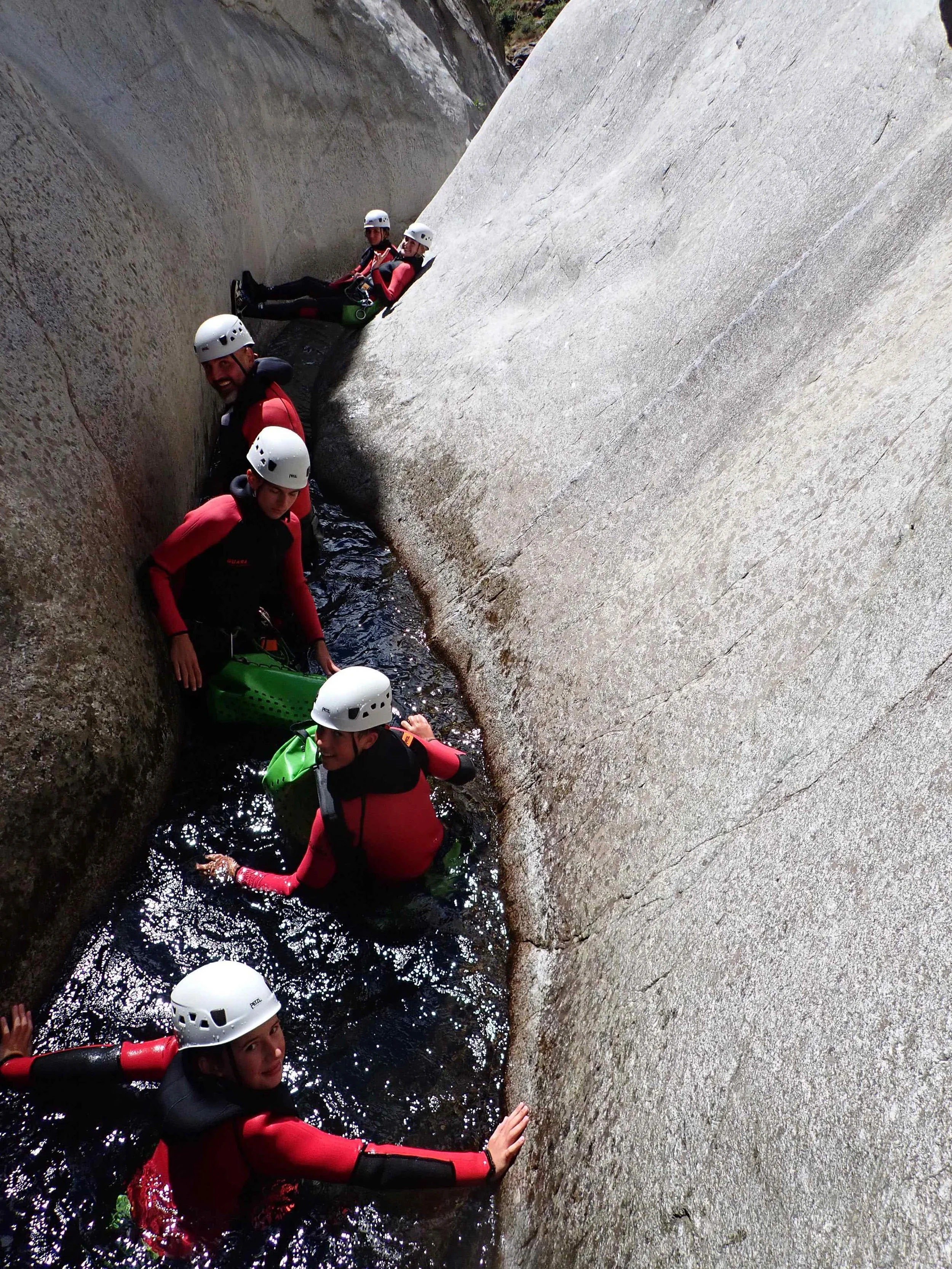 Groupe de personnes équipées de casques et de vêtements de randonnée, progressant dans une petite rivière entre de grandes falaises rocheuses.
