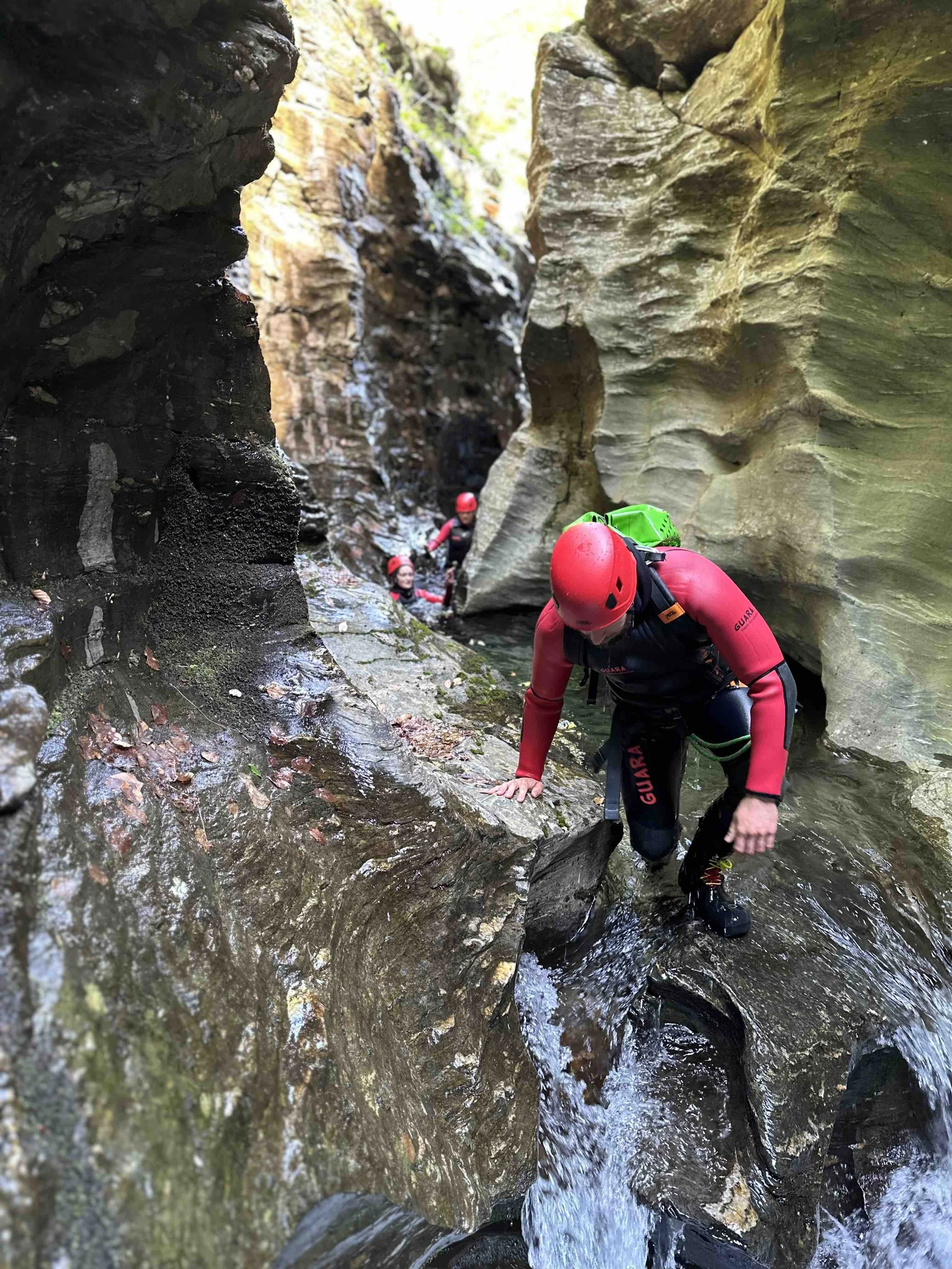 Des personnes en tenue de canyoning, portant des casques rouges, traversent une gorge rocheuse étroite en suivant un ruisseau.