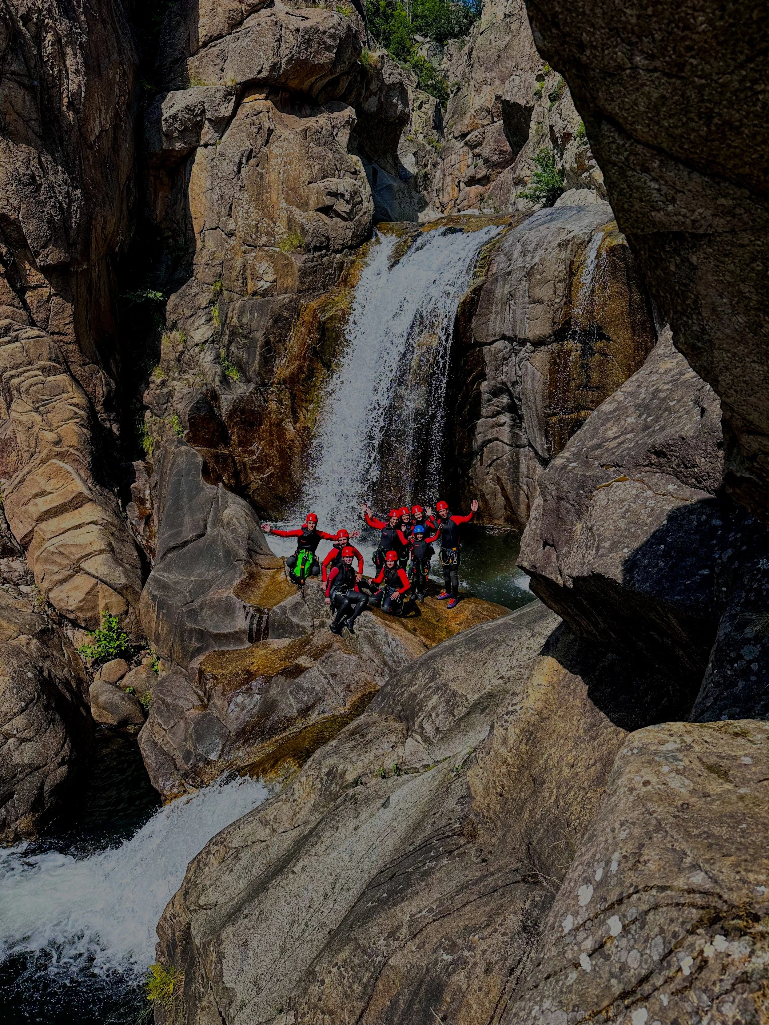 Groupe de personnes en tenue de canyoning, avec casques et équipement, posant devant une cascade rocheuse dans un canyon.