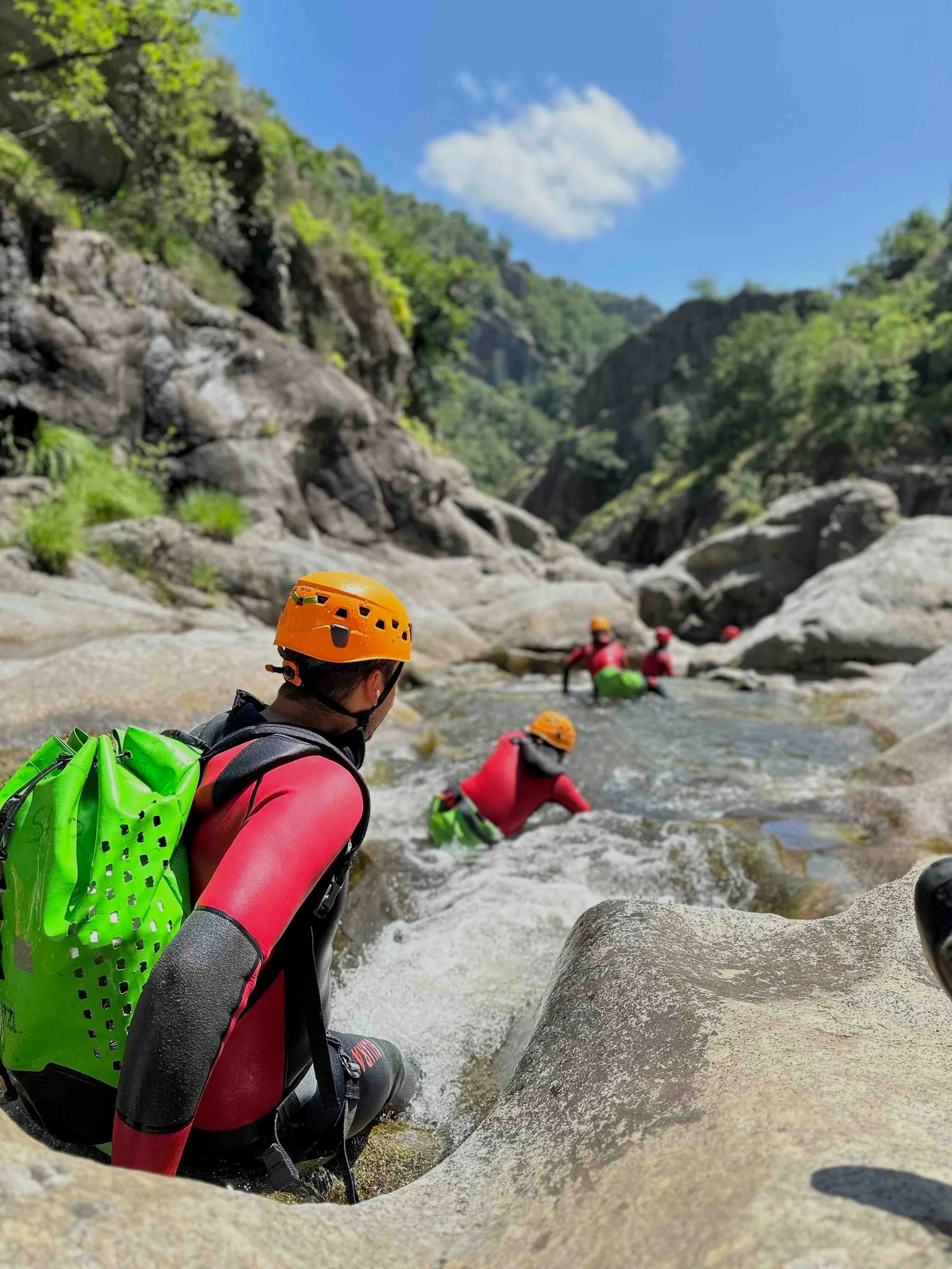Groupe de personnes en équipement d'escalade dans une rivière rocheuse en montagne sous un ciel bleu.