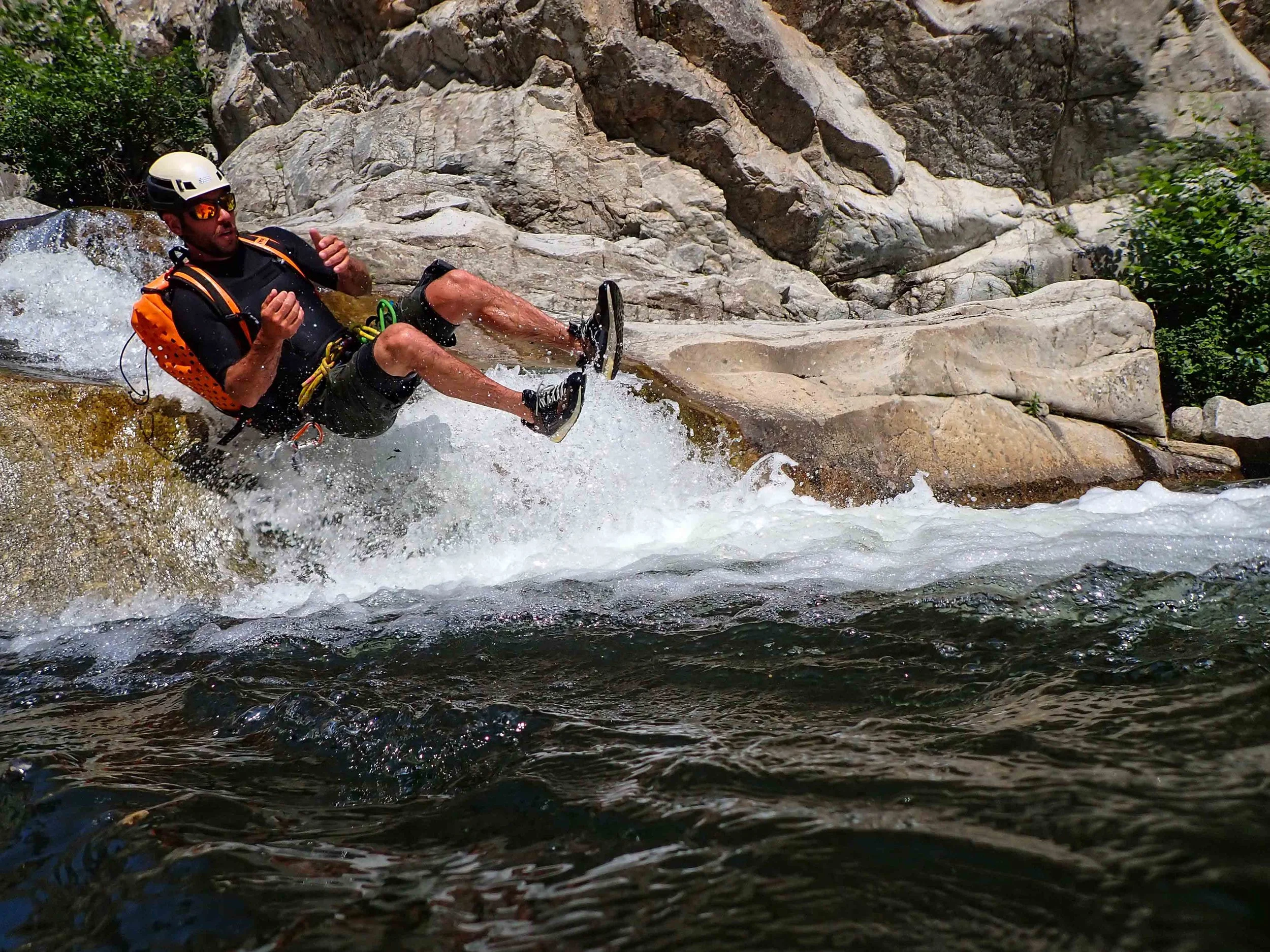 Un homme en équipement de protection, casque et gilet de sauvetage, fait du kayak en descente dans une rivière avec des rochers autour.