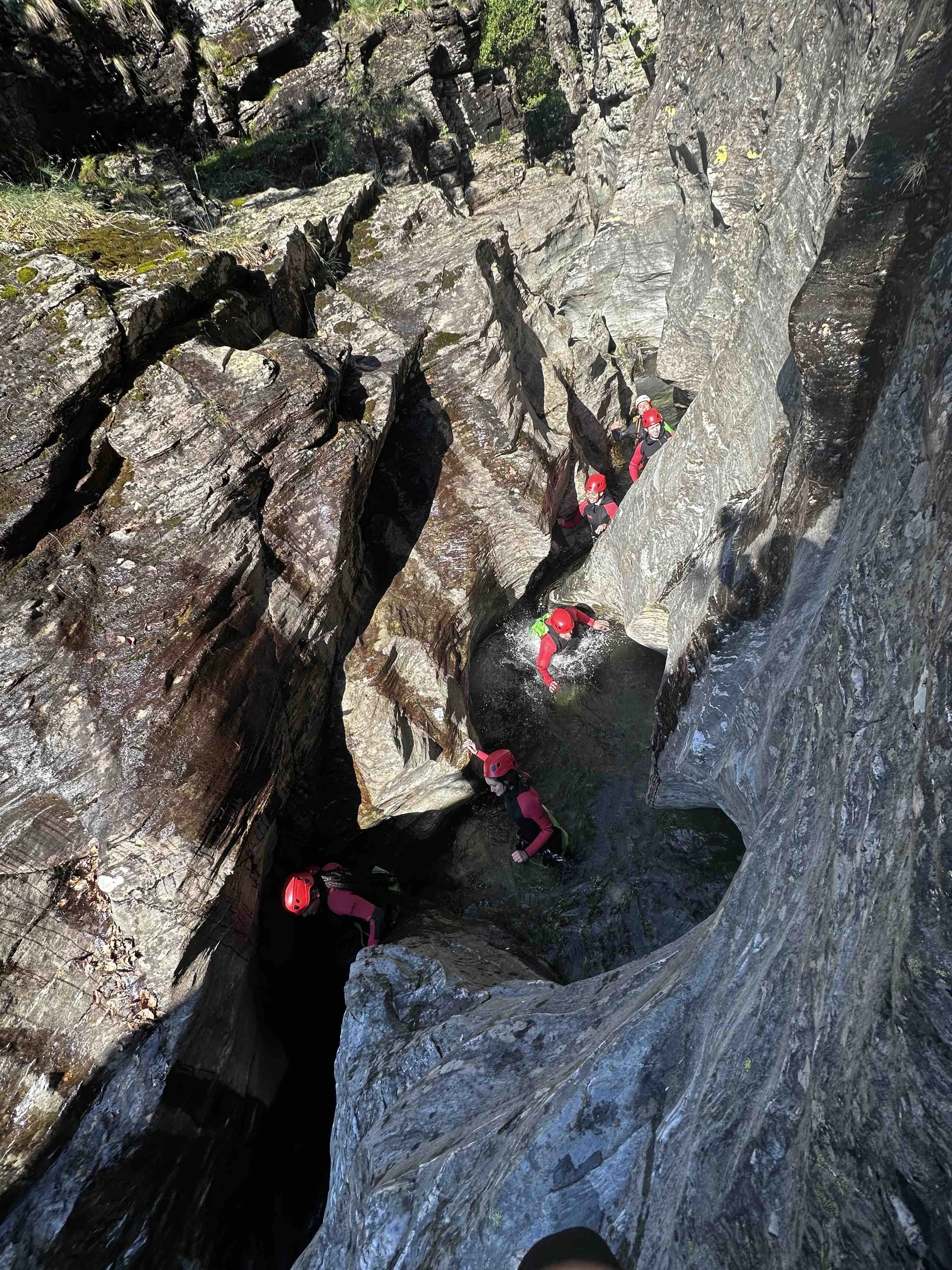 Groupe de randonneurs en escalade dans une gorge rocheuse, portant des casques rouges et des vêtements de randonnée.