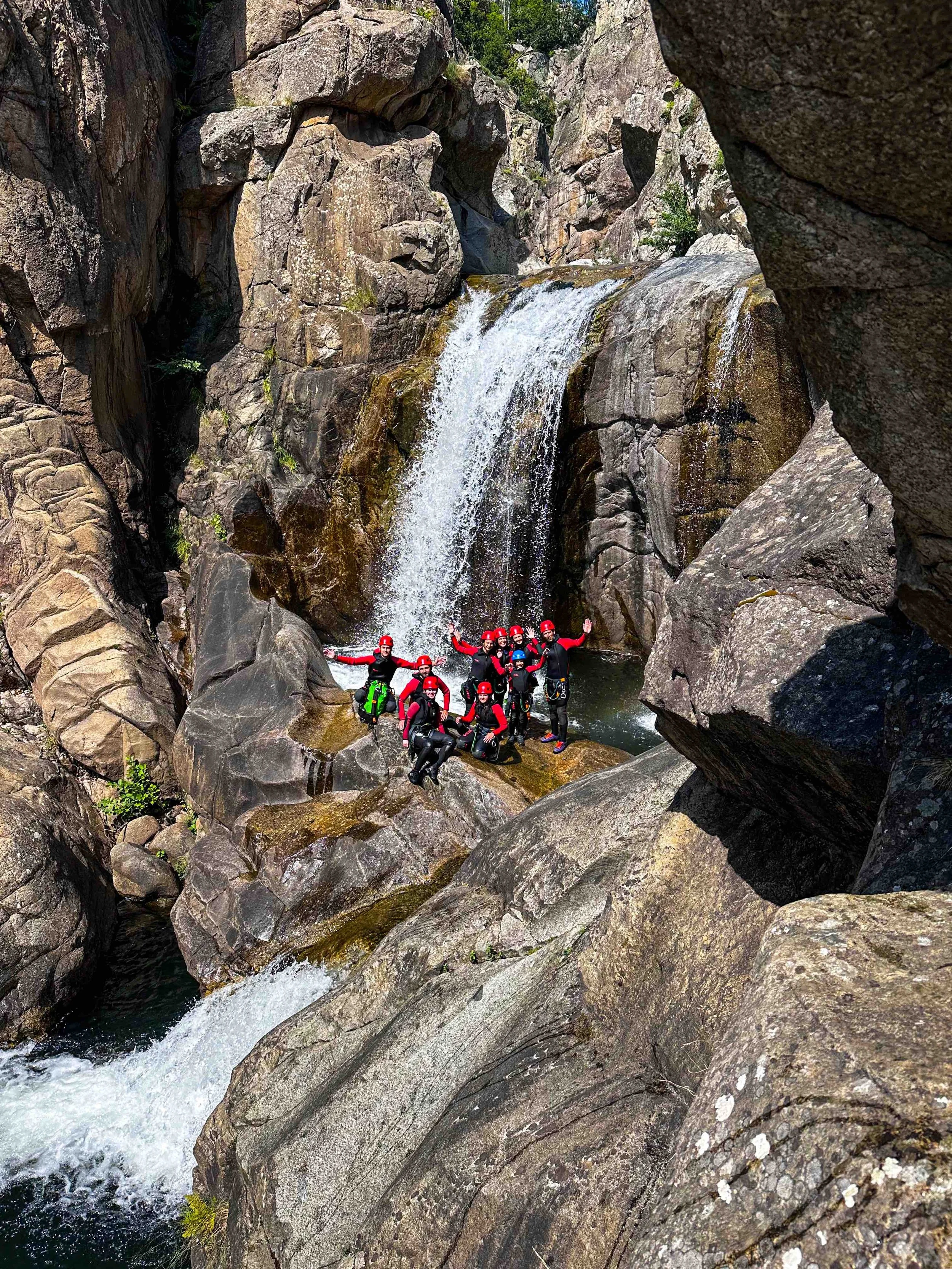 Groupe de personnes en équipement de canyoning avec casques et harnais, posant près d'une cascade rocheuse dans un canyon.