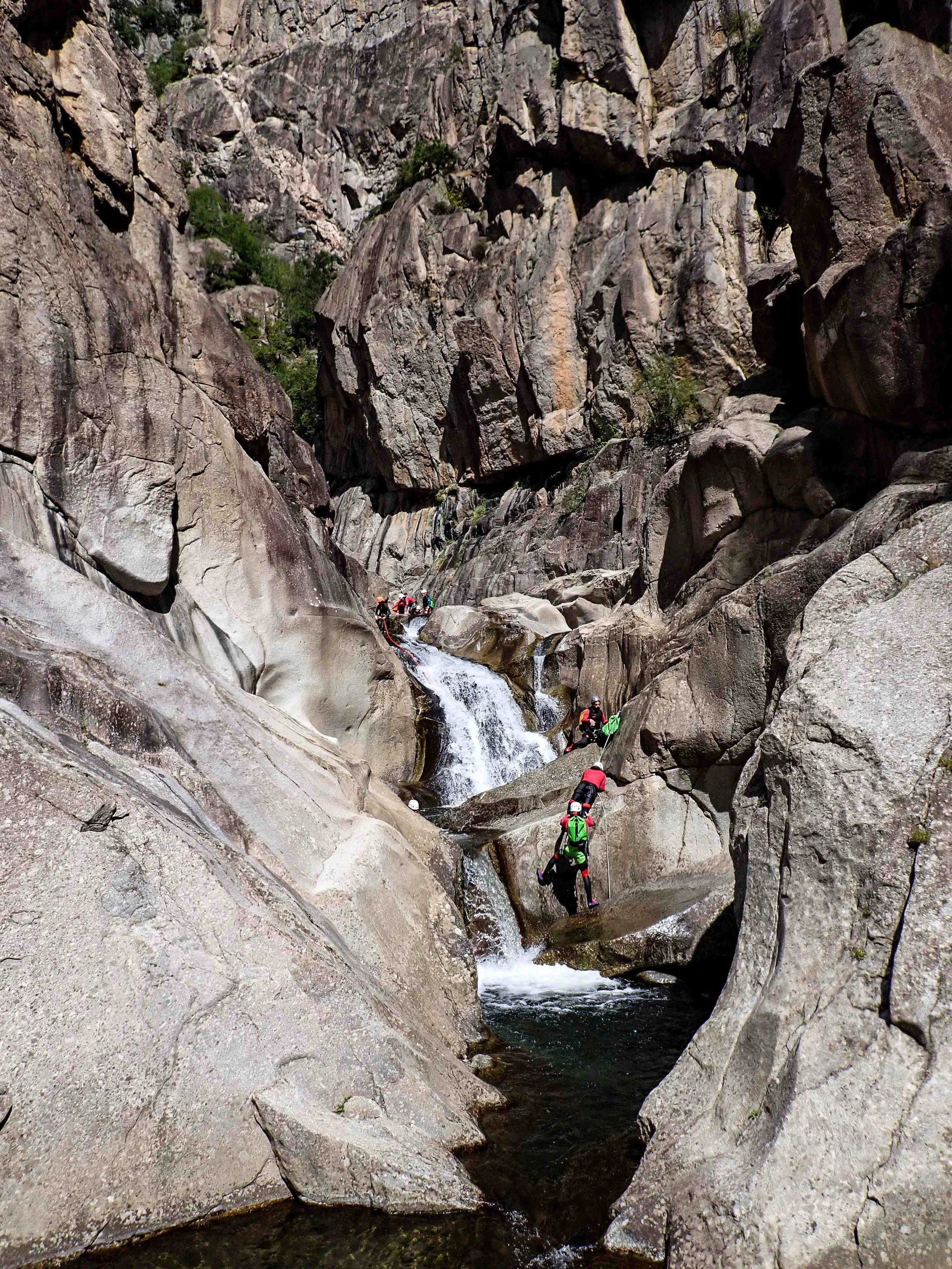 Des personnes pratiquent de la randonnée ou de l'escalade dans un canyon rocheux avec des eaux claires et des rochers escarpés.