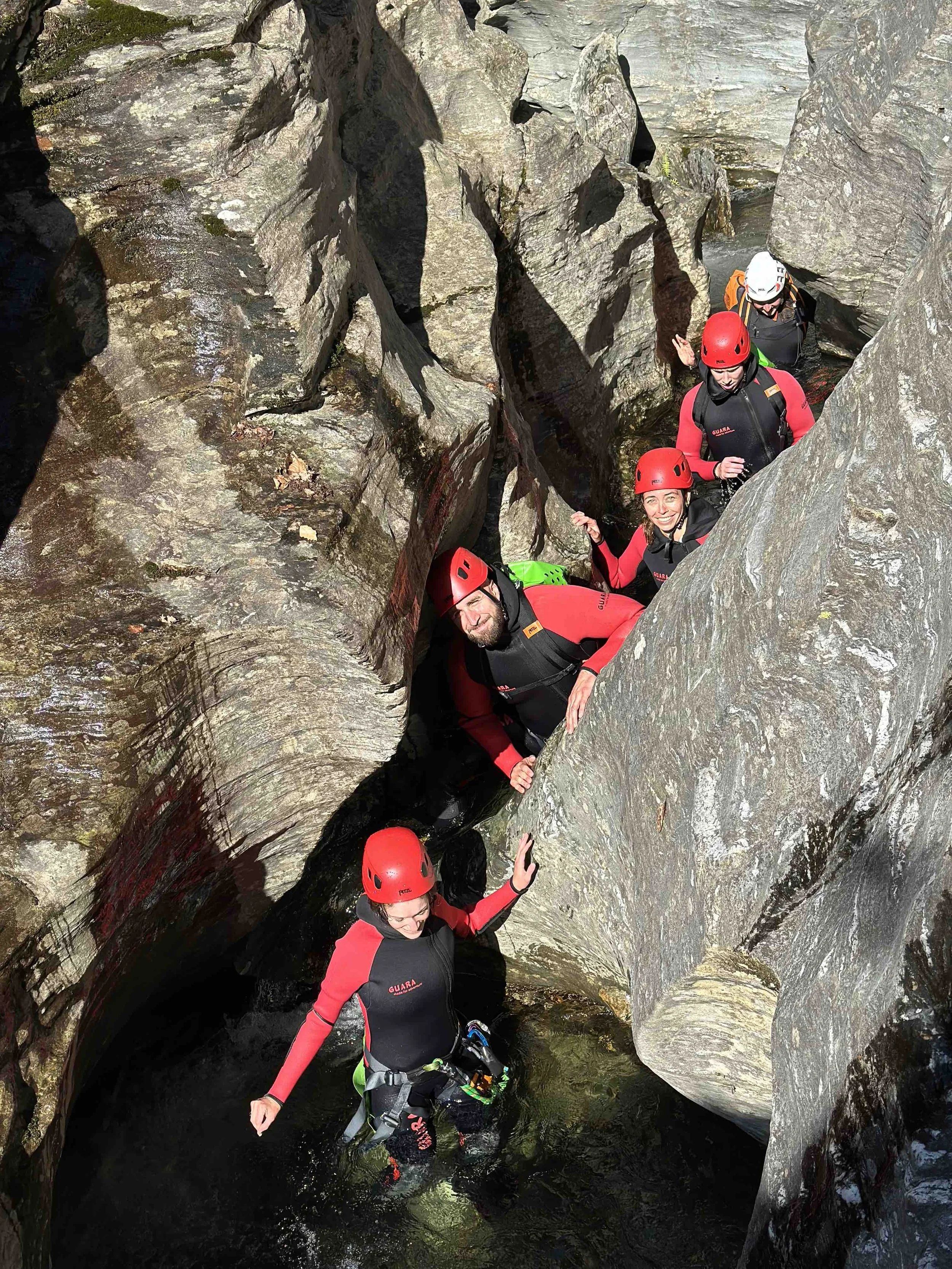 Groupe de personnes en équipement de canyoning avec casque et harnais, progressant dans une gorge rocheuse avec de l'eau.