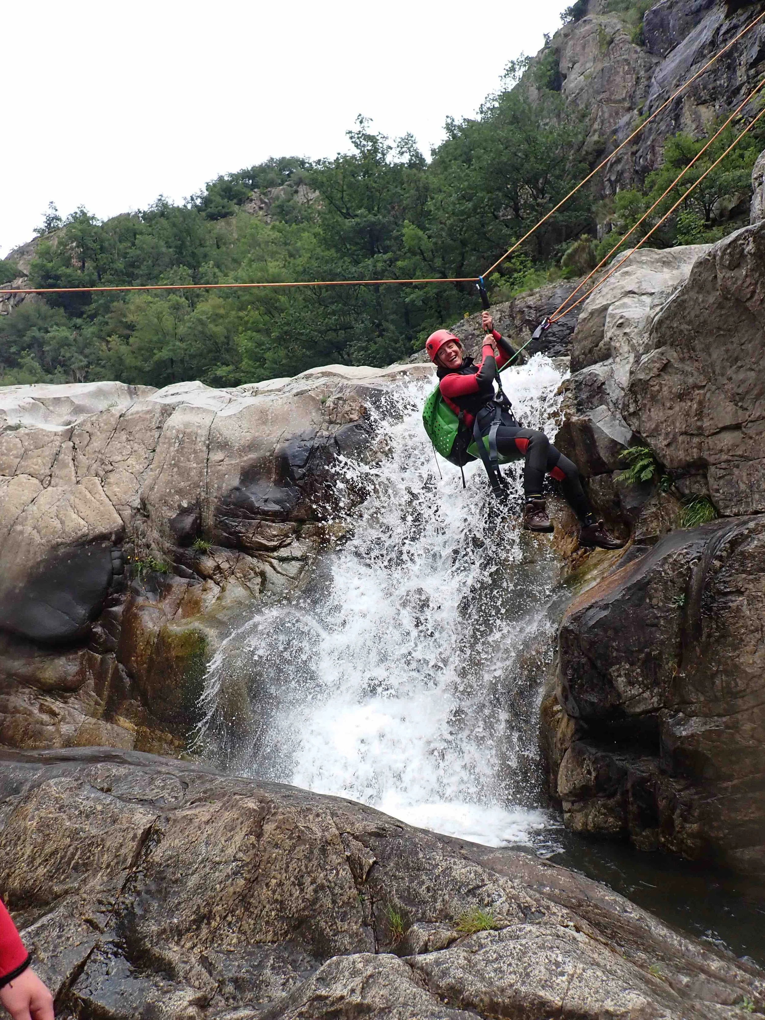 Une personne en équipement de canyoning utilise un harnais et une corde pour descendre une cascade rocheuse.