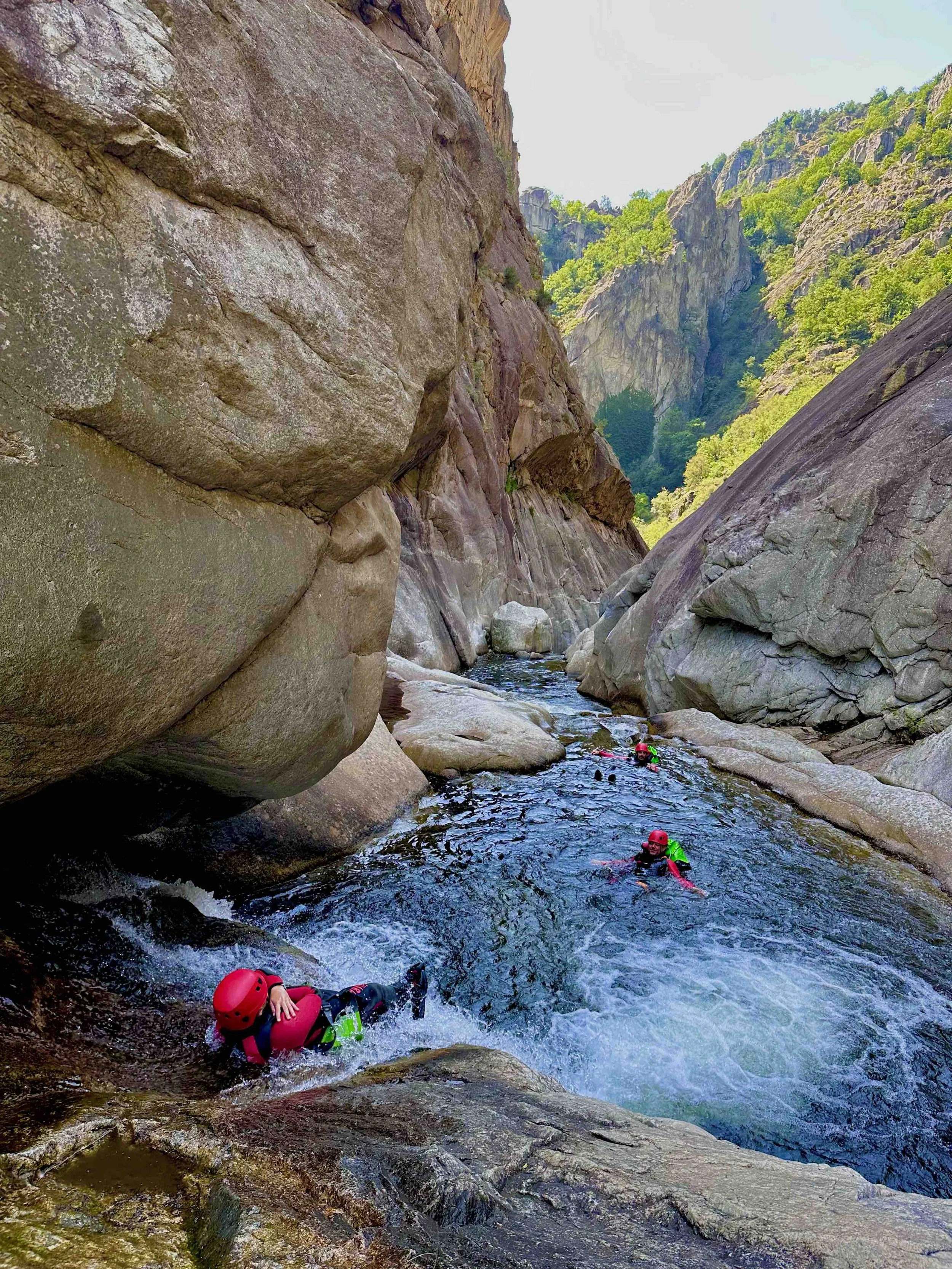 Des personnes faisant du canyionisme dans une gorge rocheuse avec des eaux vives, entourée de falaises et de végétation verte.