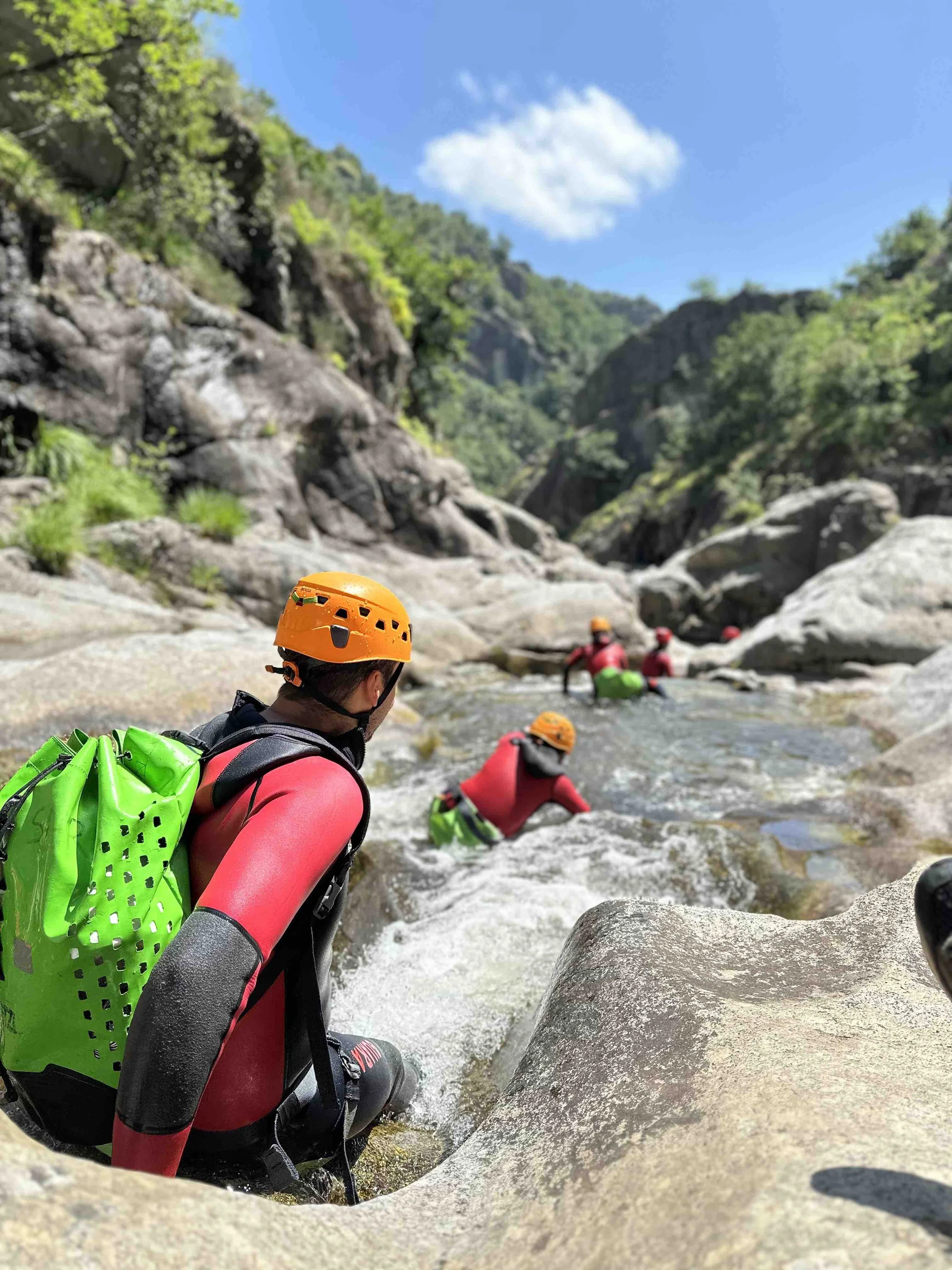 Groupe de personnes faisant de la canyoning dans une rivière bordée de rochers et de végétation sous un ciel bleu.