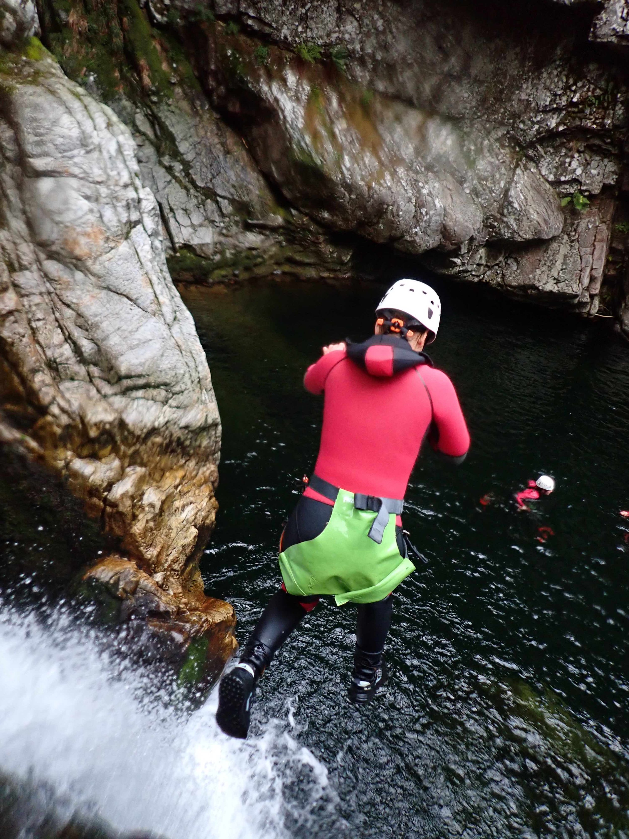 Personne portant un casque et une combinaison de protection sautant dans une rivière rocheuse durant une activité de canyoning.