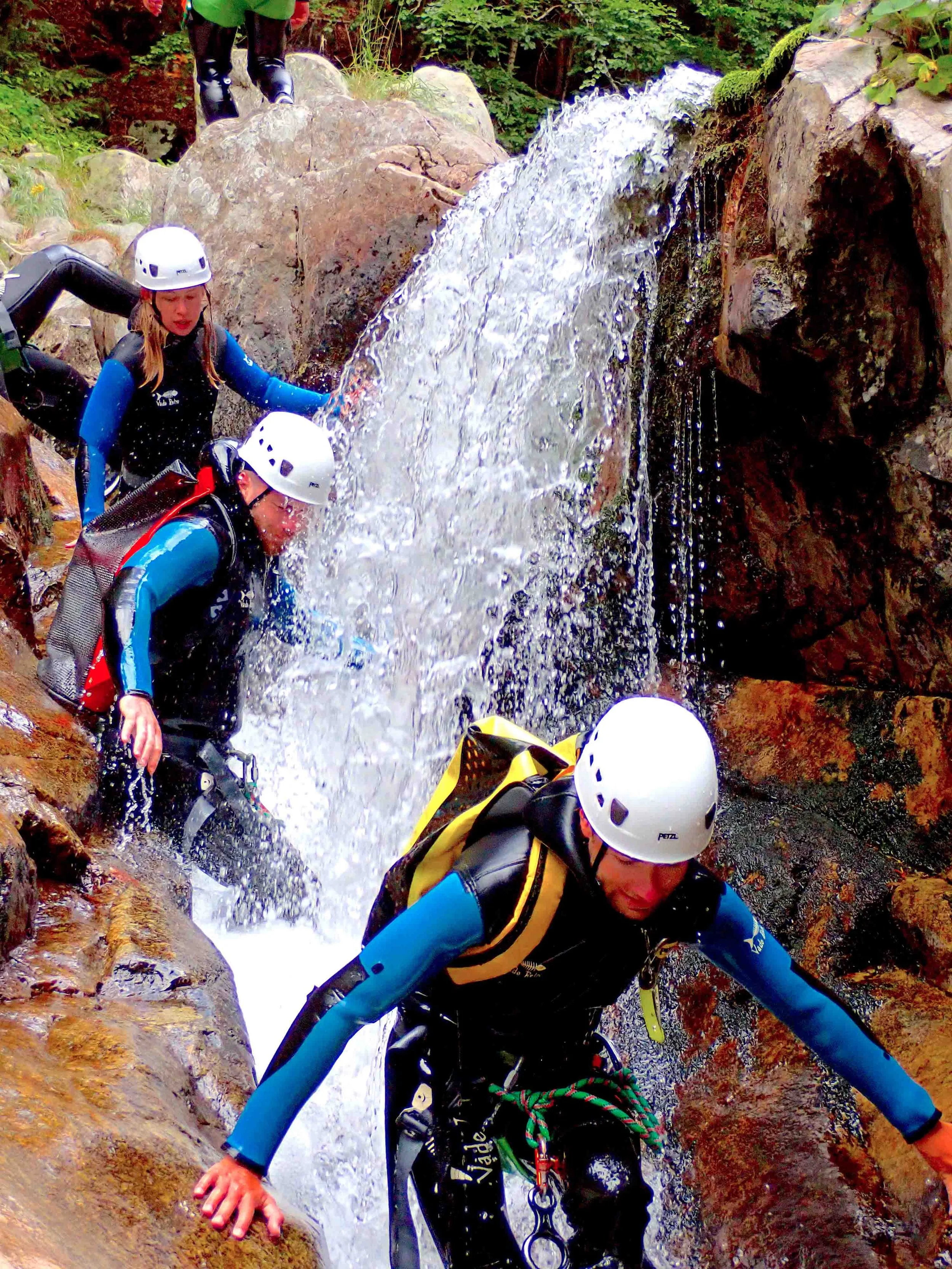 Trois personnes en équipement de canyoning, avec casque et combinaison, descendent une cascade rocheuse lors d'une aventure en plein air.