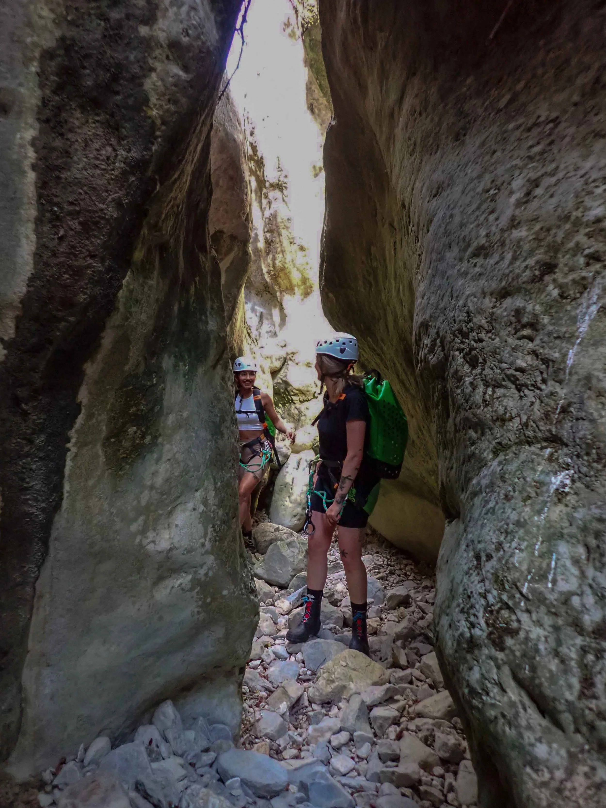 Deux femmes équipées pour l'escalade en canyon, portant des casques, des harnais et des sacs à dos, dans une gorge rocheuse étroite avec des parois rocheuses impressionnantes.