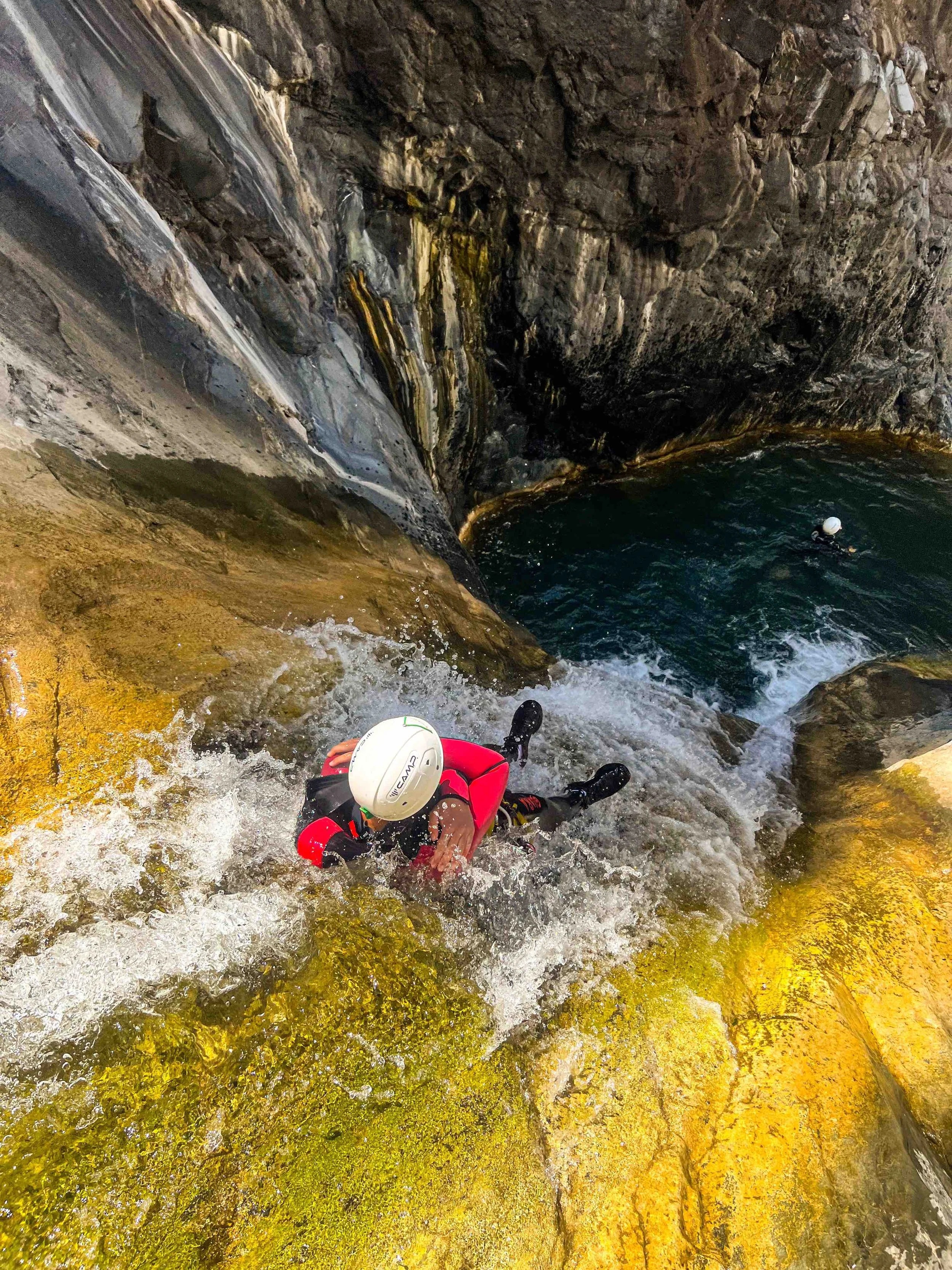 Personne en équipement de sécurité grimant une falaise rocheuse près d'une cascade ou d'une chute d'eau dans un canyon