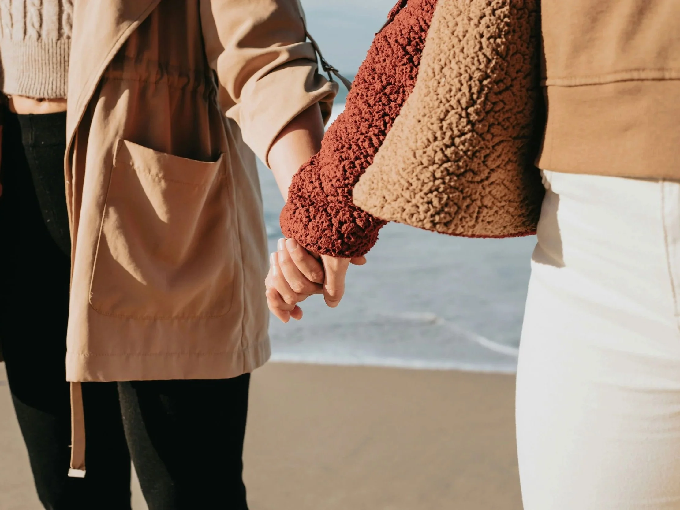 Close-up of two people holding hands on the beach, with the ocean in the background.