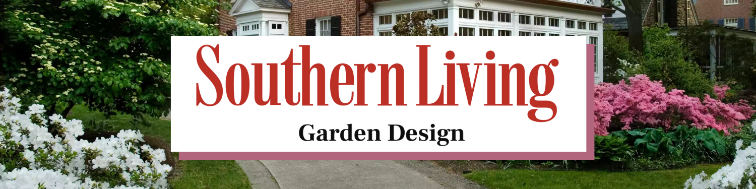 A sign that reads "Southern Living Garden Design" placed in a garden with flowering bushes and greenery in front of a house.