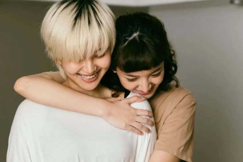 Two women are hugging each other and smiling, sharing a joyful moment.