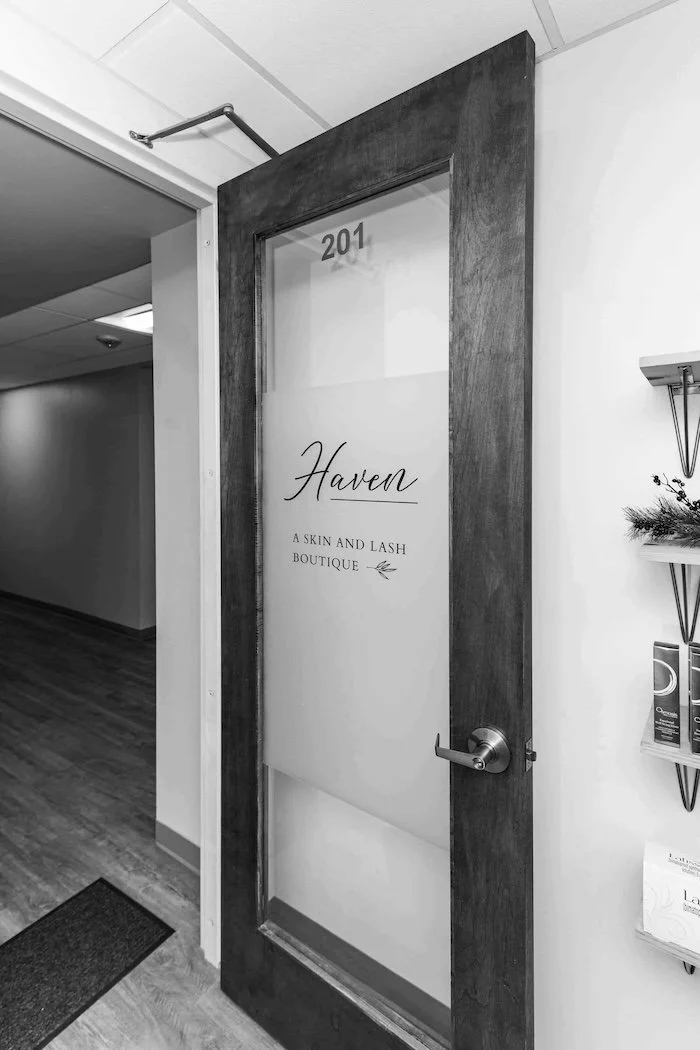 Black and white photo of a door with the number 201, labeled 'Haven A Skin and Lash Boutique', in a professional building corridor.