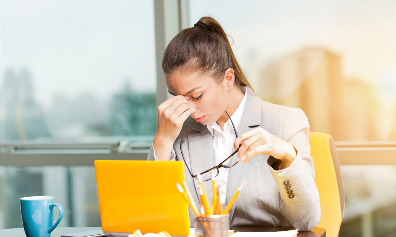 A woman sitting at a desk holding her head struggling after experiencing an emotional trigger at work.