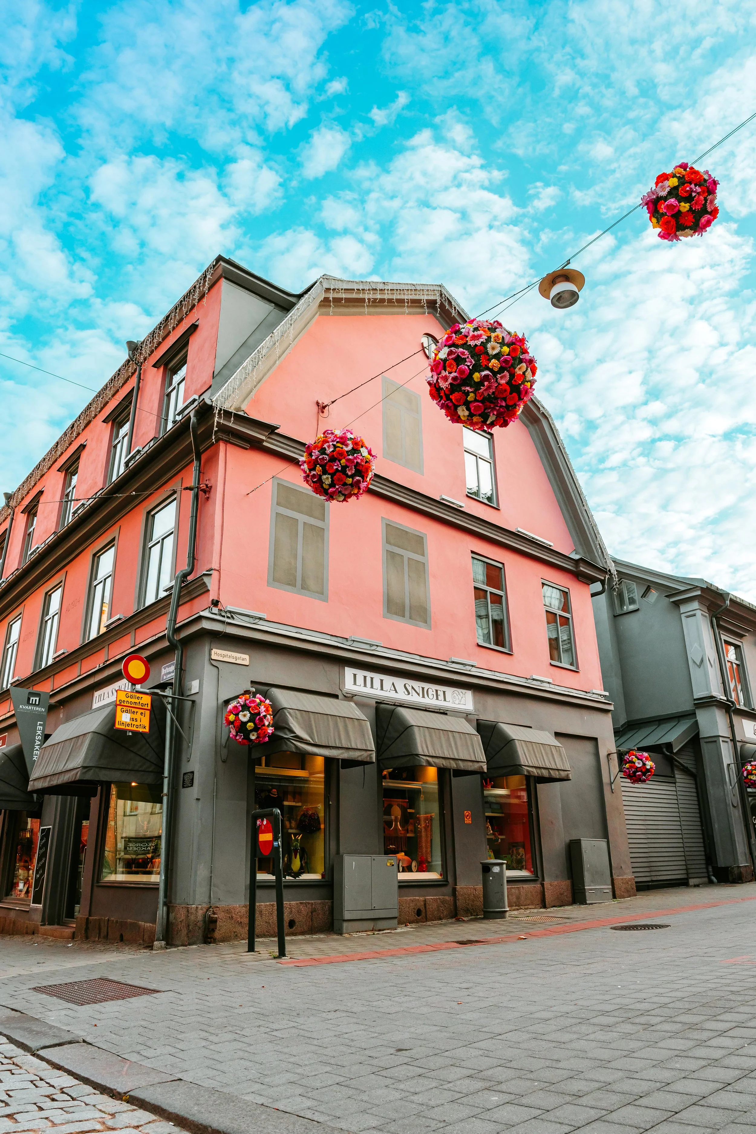 Gatusträdgård med en rosa byggnad, blomsterdekorationer och skyltfönster.