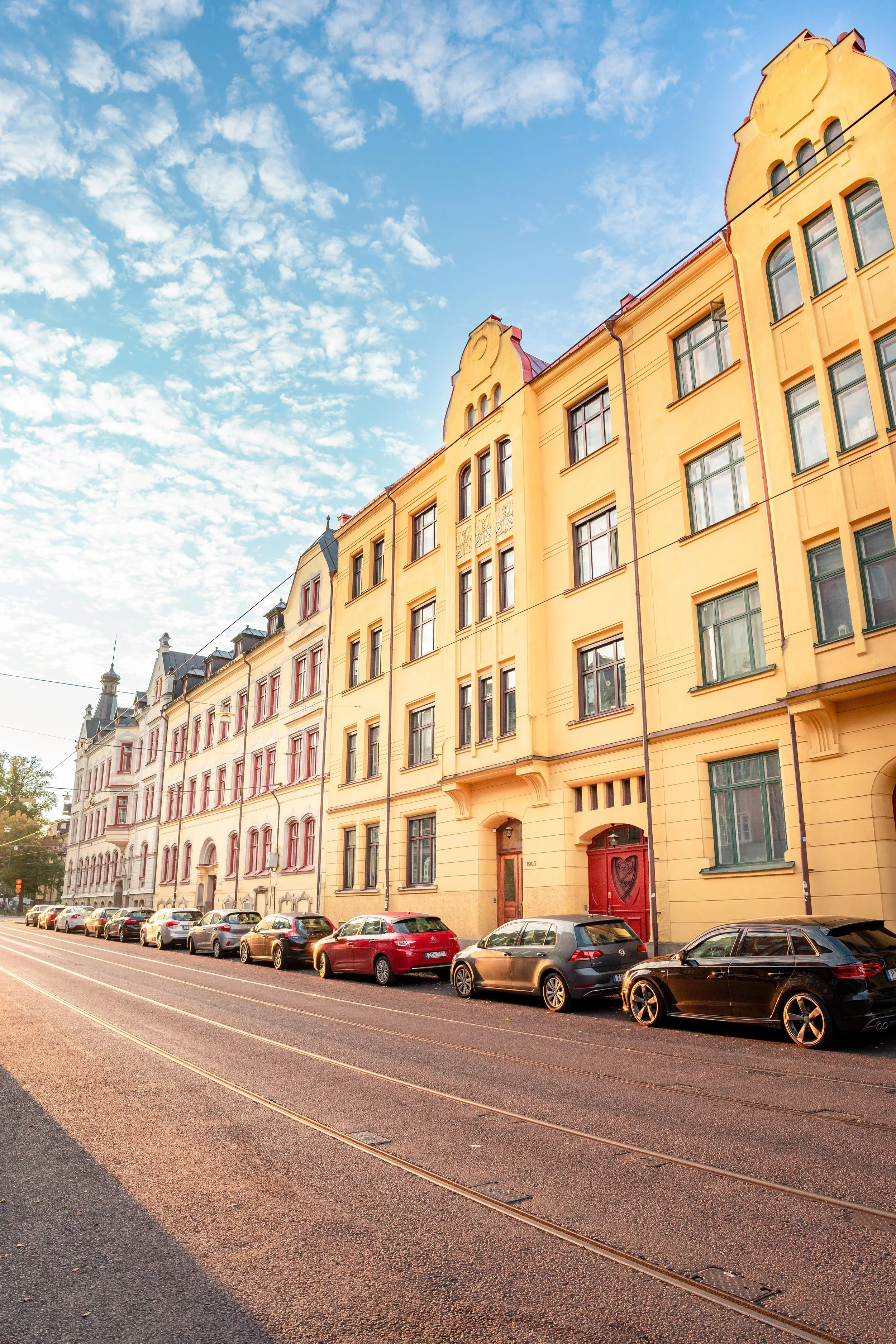 Gulaktig fasad på flerbostadshus med många fönster och bilar parkerade längs gatan, under en blå himmel med lätta moln. Stadsbild från Norrköping, fotograferad av BKMEDIA, Badi Khwies.