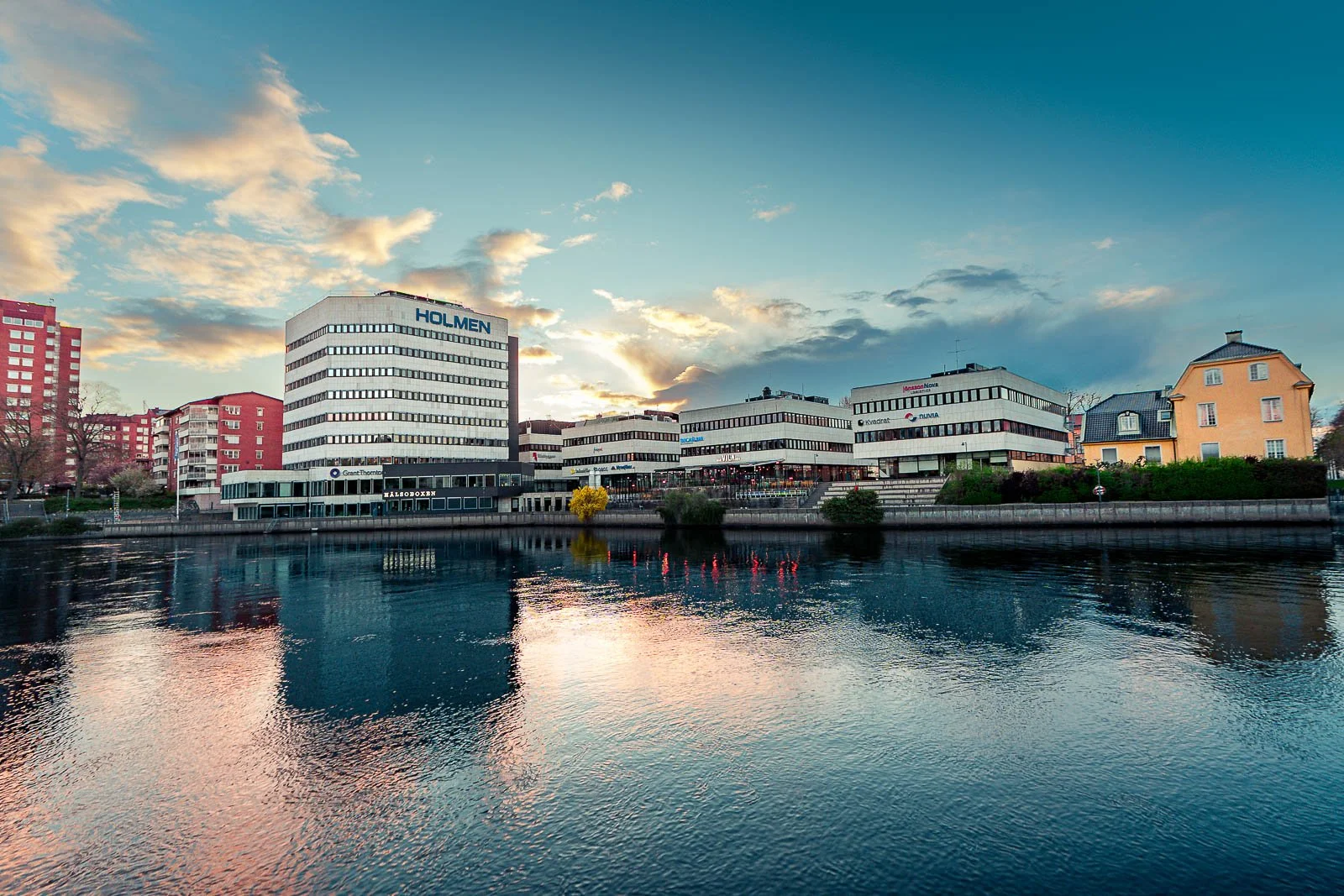 Stadsbild från Norrköping, fotograferad av BKMEDIA, Badi Khwies. Bilden visar Holmenområdet vid Motala ström med stadens byggnader, vattenspeglingar och kvällshimmel. Visuellt innehåll för platsmarknadsföring och destinationer