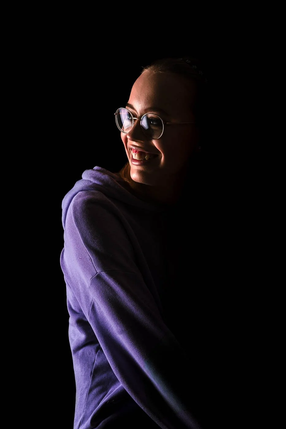 Porträttfoto i studiokänsla, fotograferat av BKMEDIA, Badi Khwies. Bilden visar ett uttrycksfullt porträtt med mörk bakgrund, riktat ljus och ett naturligt leende. Visuellt innehåll för porträtt, kreativa projekt och personlig kommunikation.