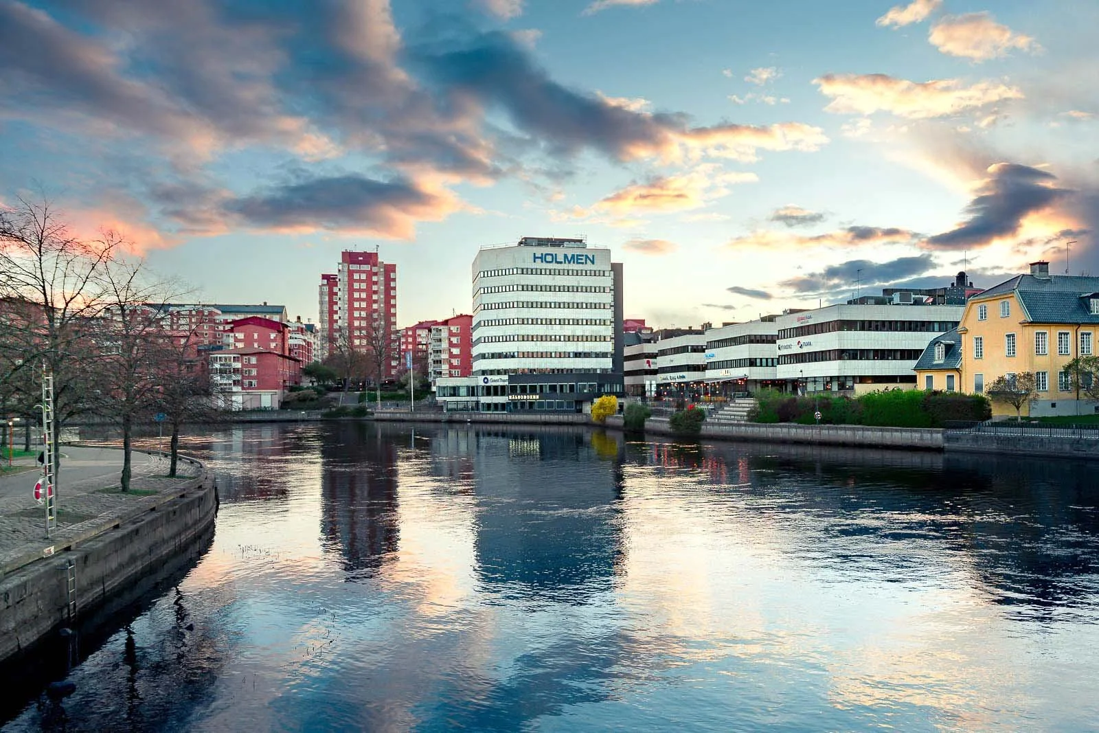 Stadslandskap från Norrköping, fotograferat av BKMEDIA, Badi Khwies. Bilden visar Holmenområdet vid Motala ström med vattenspeglingar, stadssiluett och dramatisk kvällshimmel. Visuellt innehåll för platsmarknadsföring och destinationer