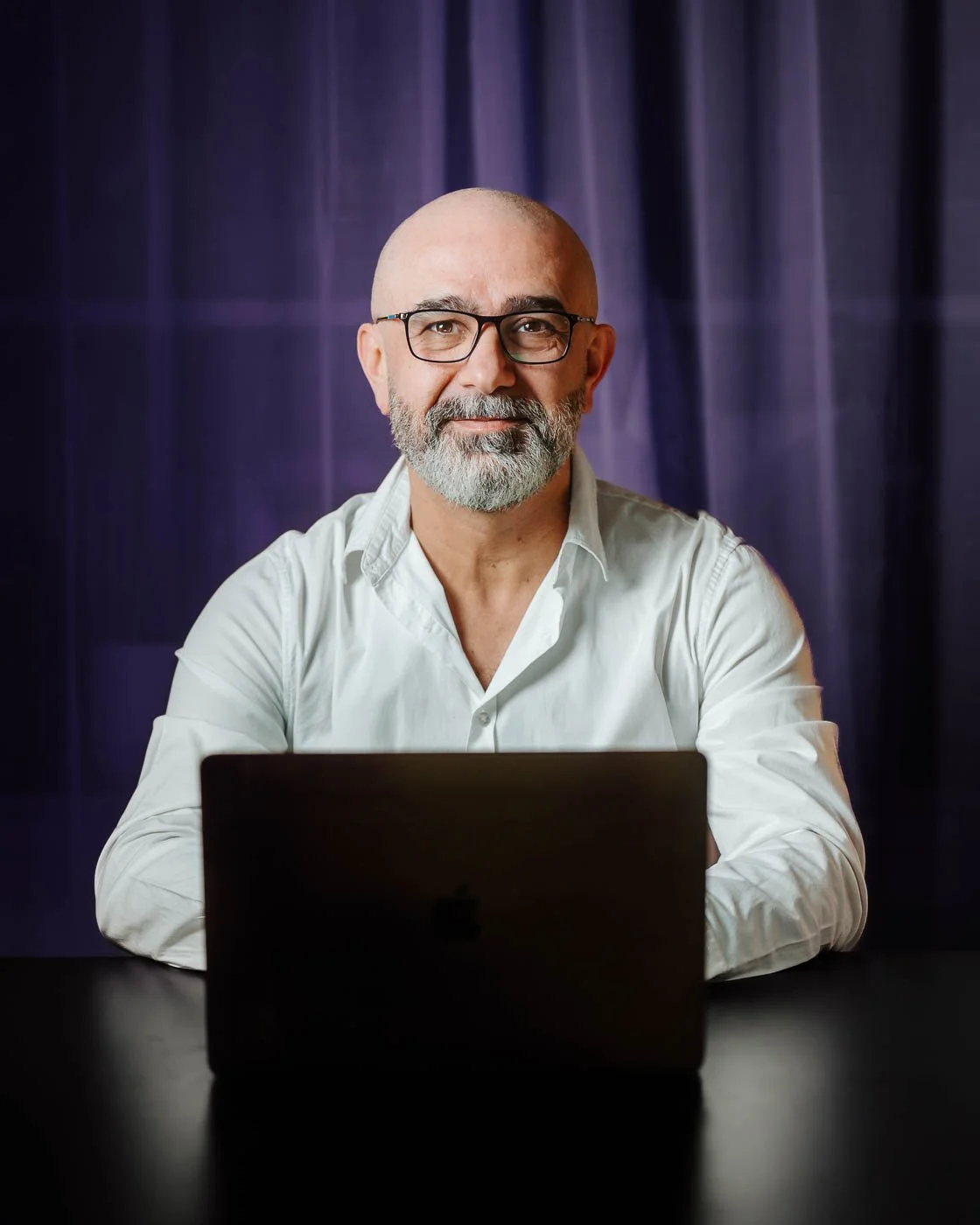 Porträttfoto för professionell profil, fotograferat av BKMEDIA, Badi Khwies. Bilden visar en person vid laptop med varm ljussättning, mörk bakgrund och tryggt uttryck. Visuellt innehåll för företagsporträtt, personligt varumärke.