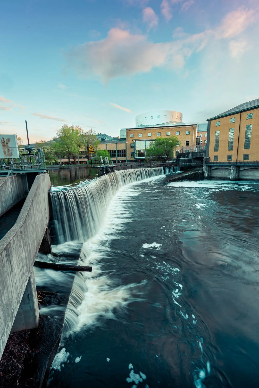 Stadsbild från Norrköping, fotograferad av BKMEDIA Fotograf: Badi Khwies. Bilden visar vattenfallet vid Motala ström med industrilandskap och Louis De Geer Konsert & Kongress i bakgrunden. Skapad för platsmarknadsföring och destinationer.