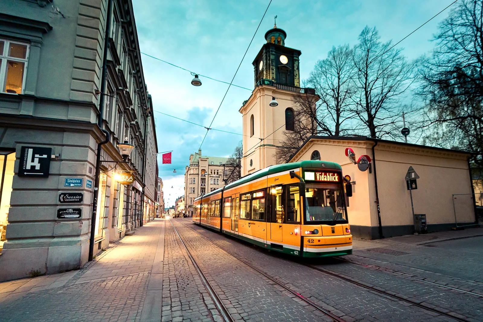 Stadsbild från Norrköping, fotograferad av BKMEDIA Fotograf: Badi Khwies. Bilden visar Norrköpings klassiska gula spårvagn på Drottninggatan, omgiven av stenlagda gator och historisk arkitektur. Skapad för platsmarknadsföring och destinationer.