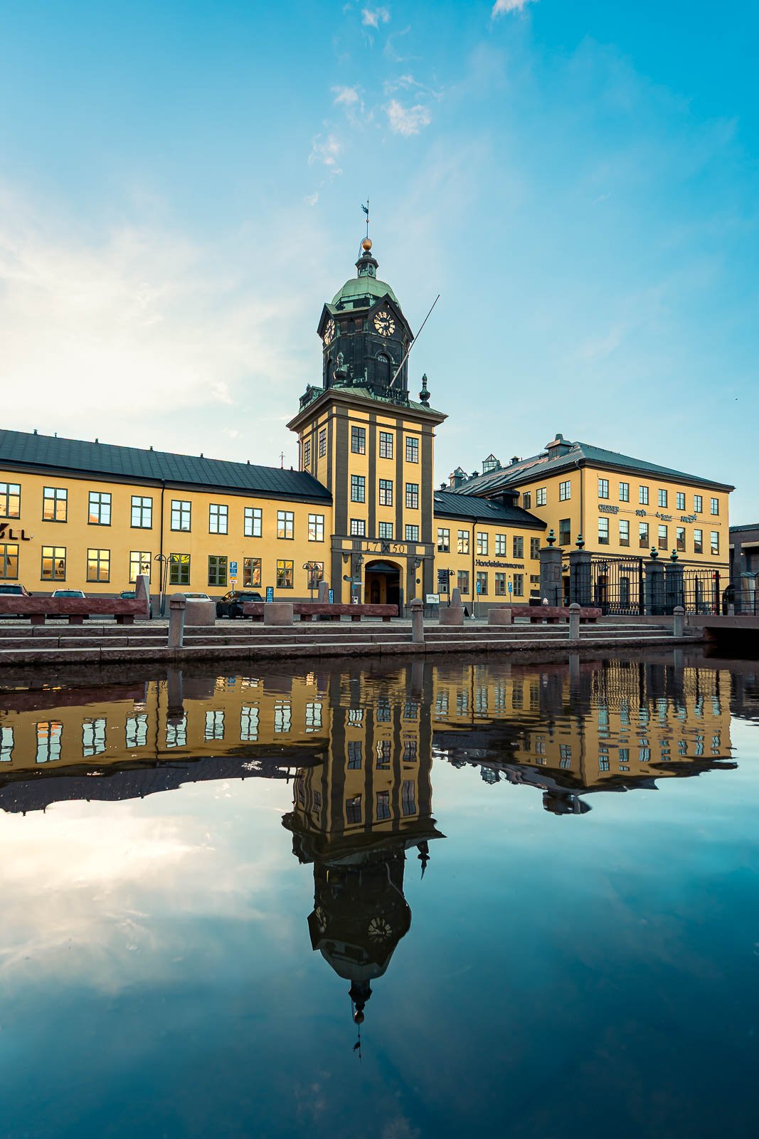 En stadsvy med en gul byggnad och ett torn med en klocka, reflekterad i vattnet foran.