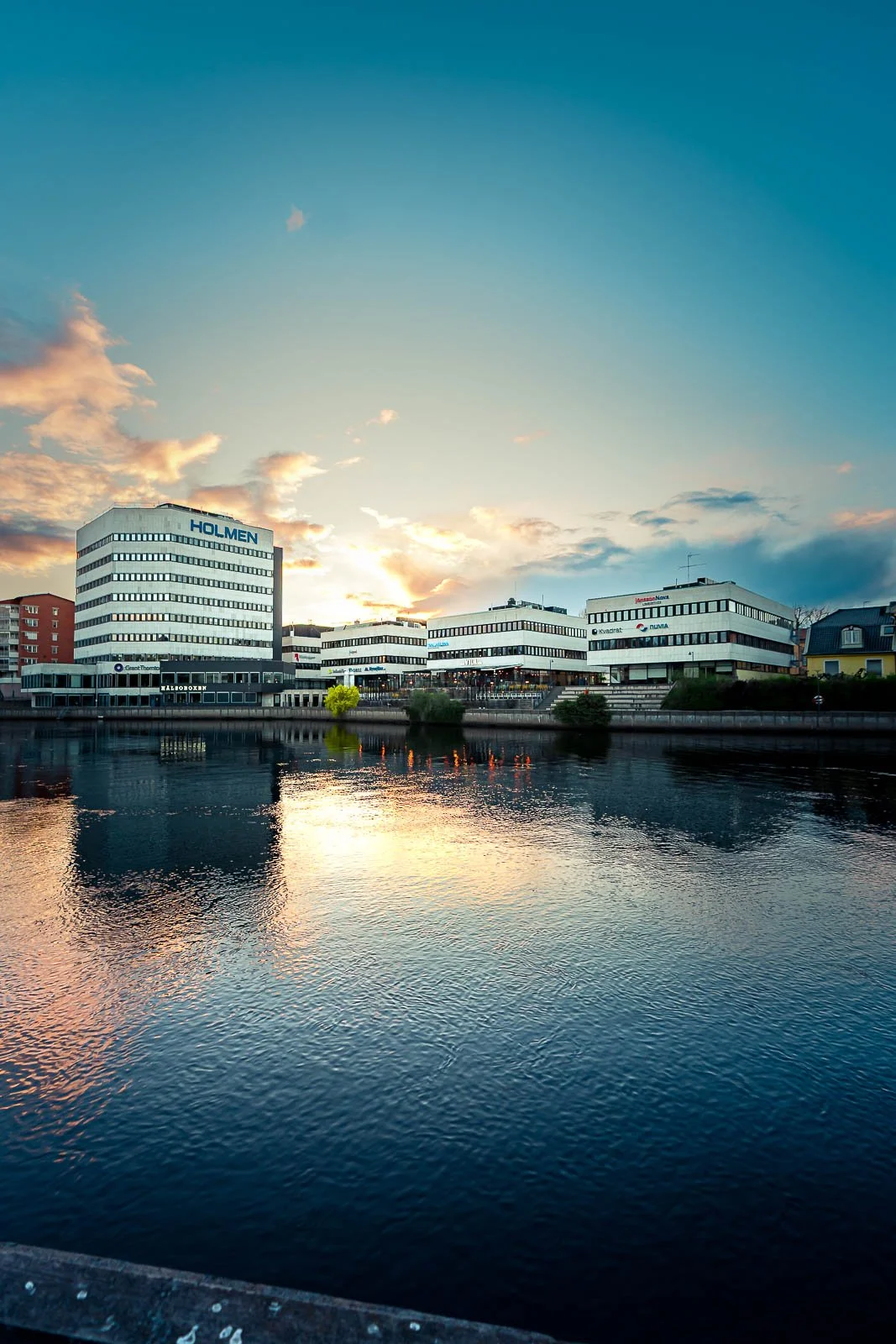 Moderna vita kontorsbyggnader vid vatten under en solnedgång i en stad.
