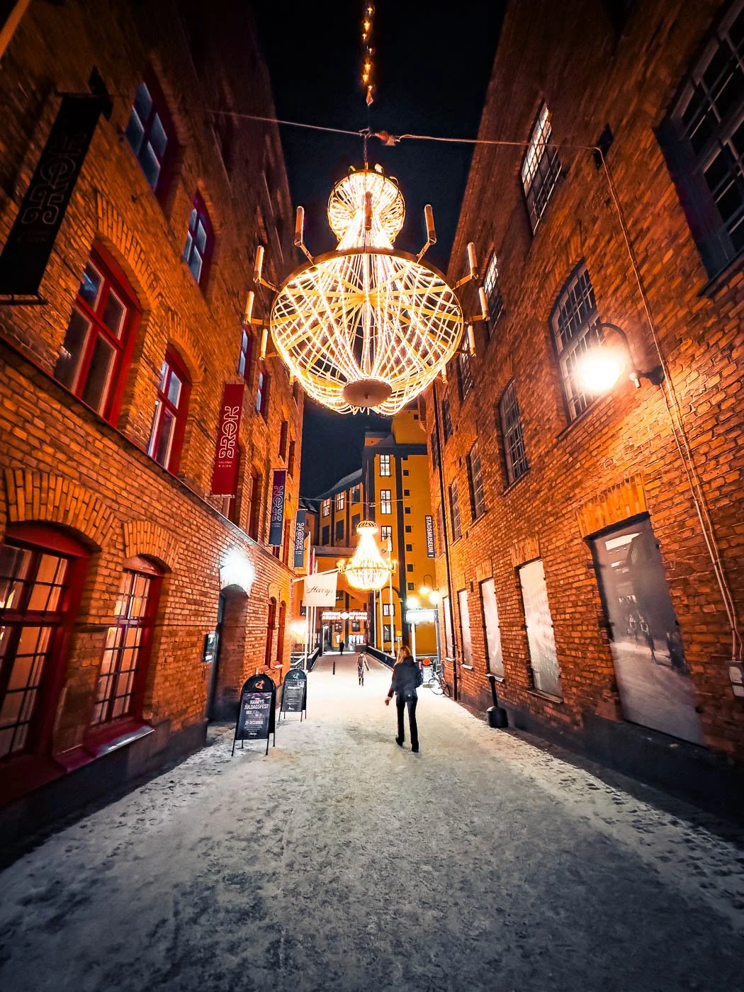 Stadsbild från Norrköping, fotograferad av BKMEDIA Fotograf: Badi Khwies. Bilden visar en upplyst gränd i Industrilandskapet med tegelbyggnader, snö och varm kvällsatmosfär. Skapad för platsmarknadsföring och destinationer