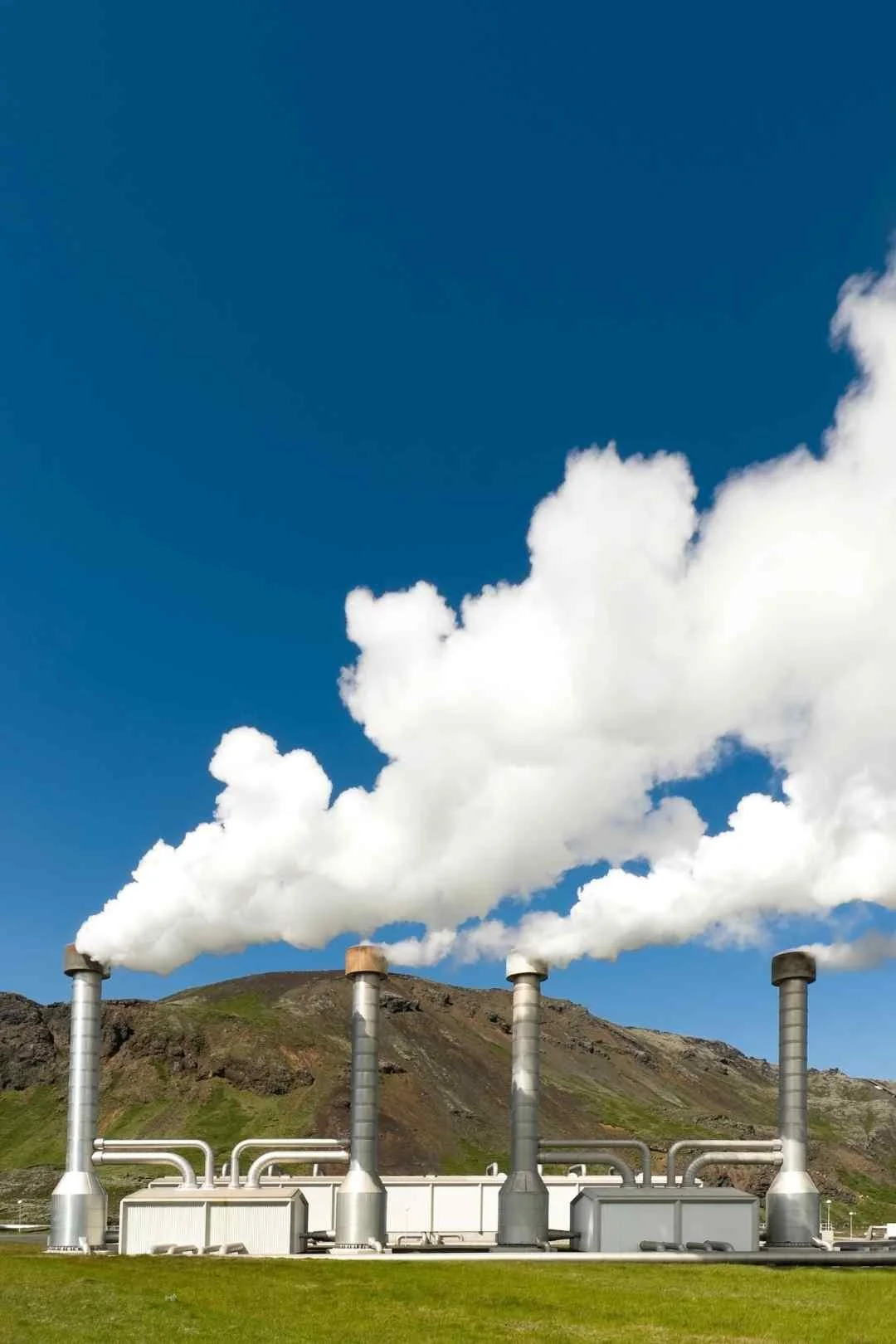 A geothermal plant with steam in front of a mountain.