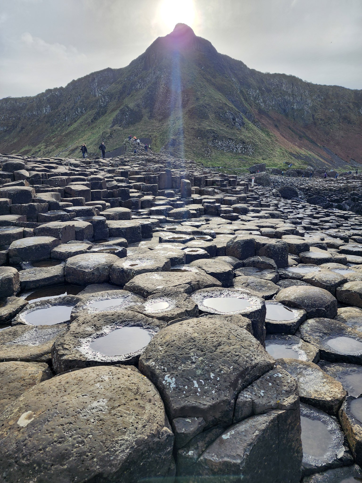 The sun peeks out above a mountain top at Giant's Causeway in Ireland.