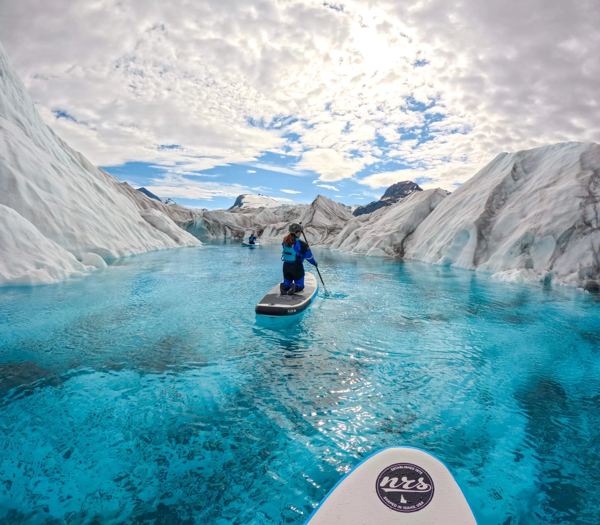 Girl paddleboaring in bright blue water surrounded by ice.